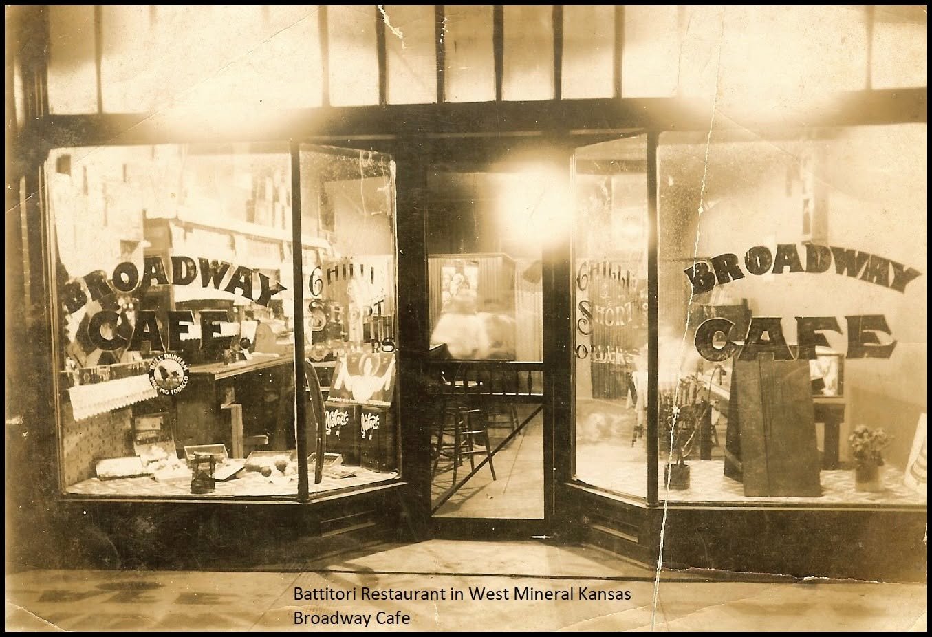 Vintage photo of the entrance to Brittany Restaurant and Broadway Cafe in West Mineral, Kansas, showing glass windows with signs and reflections of the street.