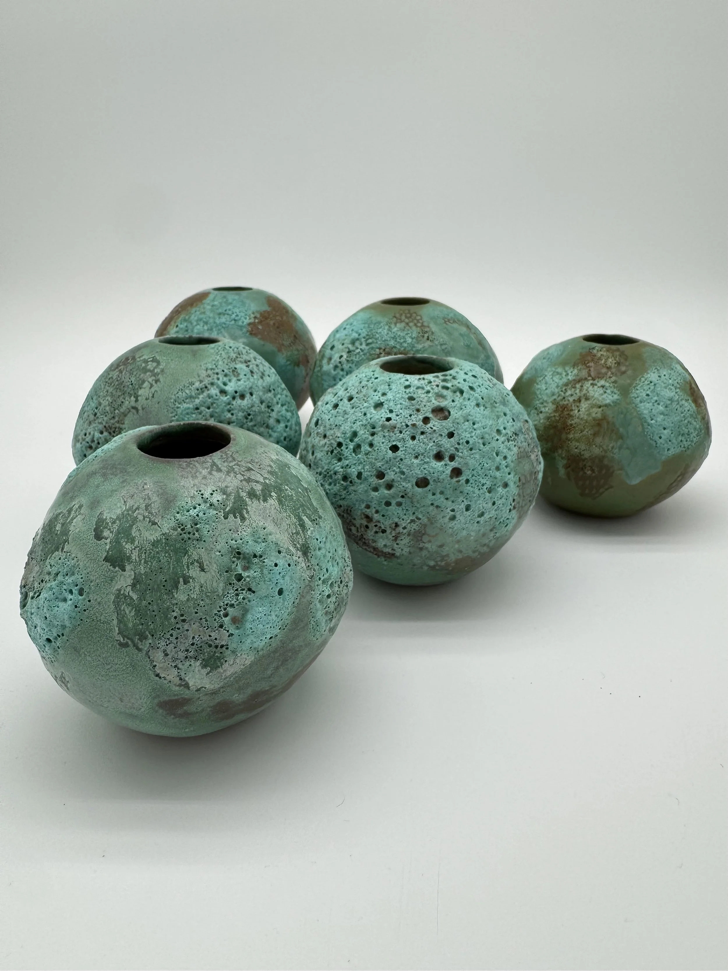 Six round turquoise ceramic vases with textured and glazed surfaces, arranged together on a white background.