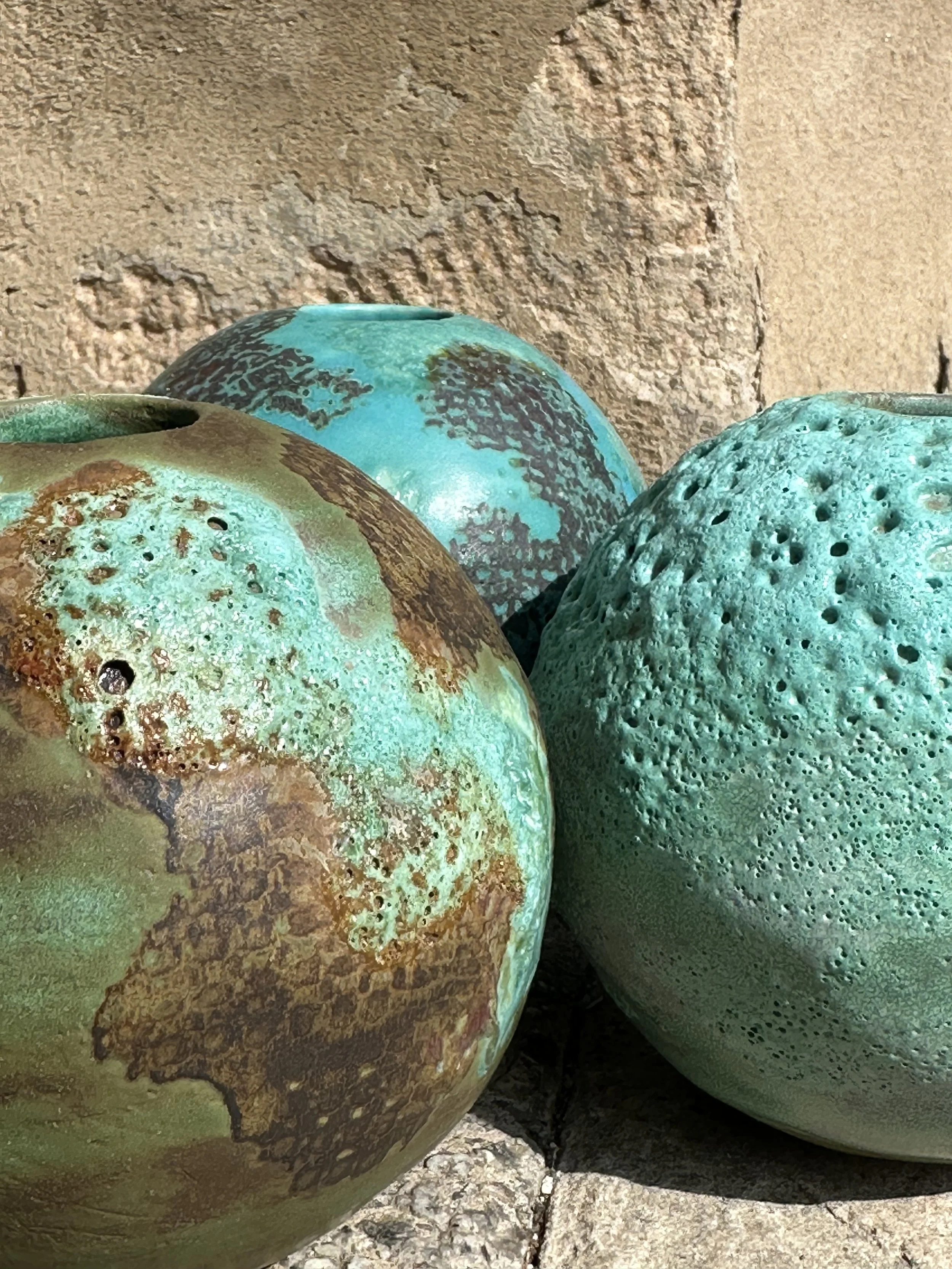 Close-up of colorful weathered ceramic garden spheres with textured surfaces and cracks, placed outdoors on a stone surface against a rough wall.