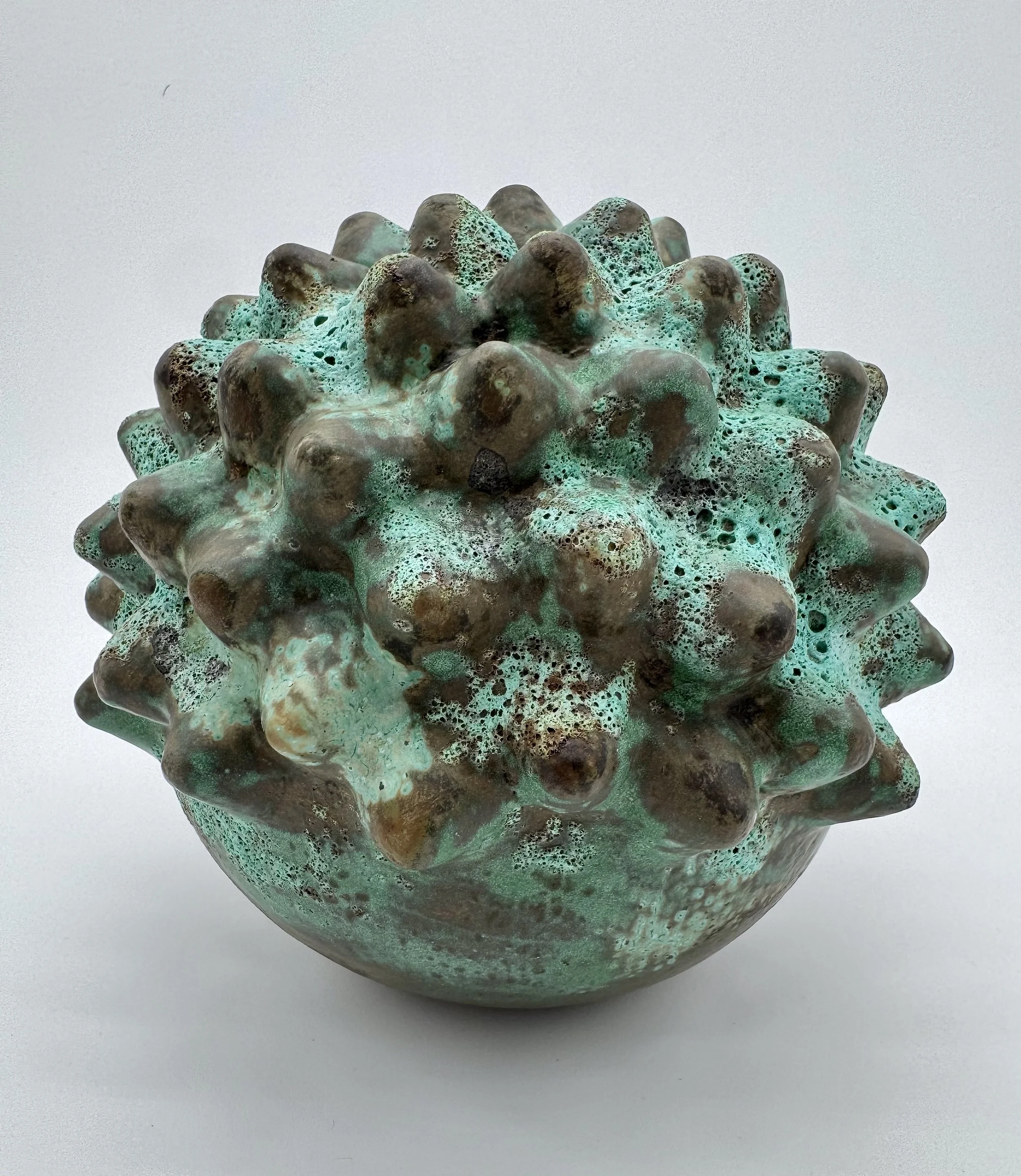 Close-up of a spherical decorative object with a textured surface resembling coral or encrusted rock, predominantly light green with brown patches.