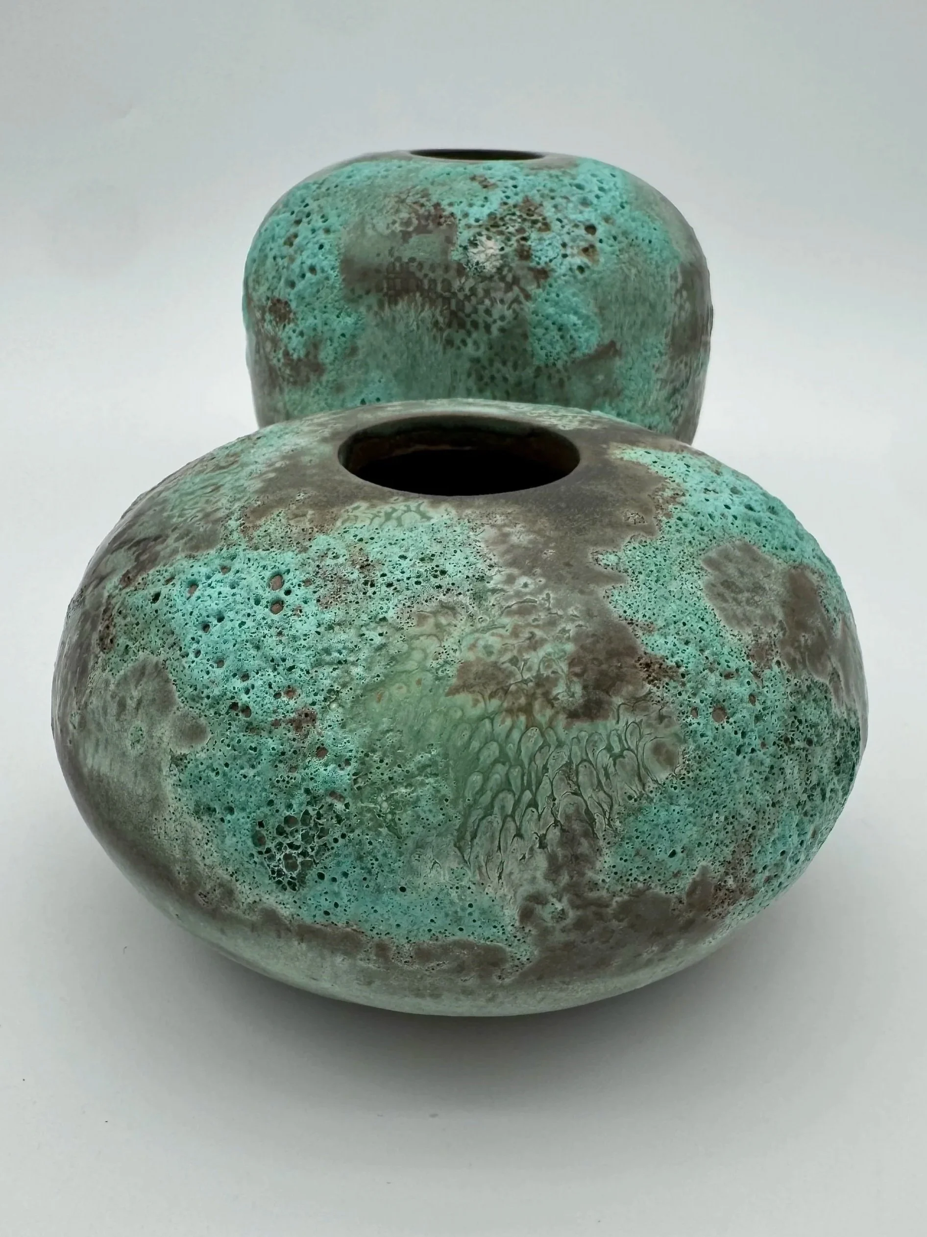 Two ceramic vases with textured, green and brown glaze on a white surface.