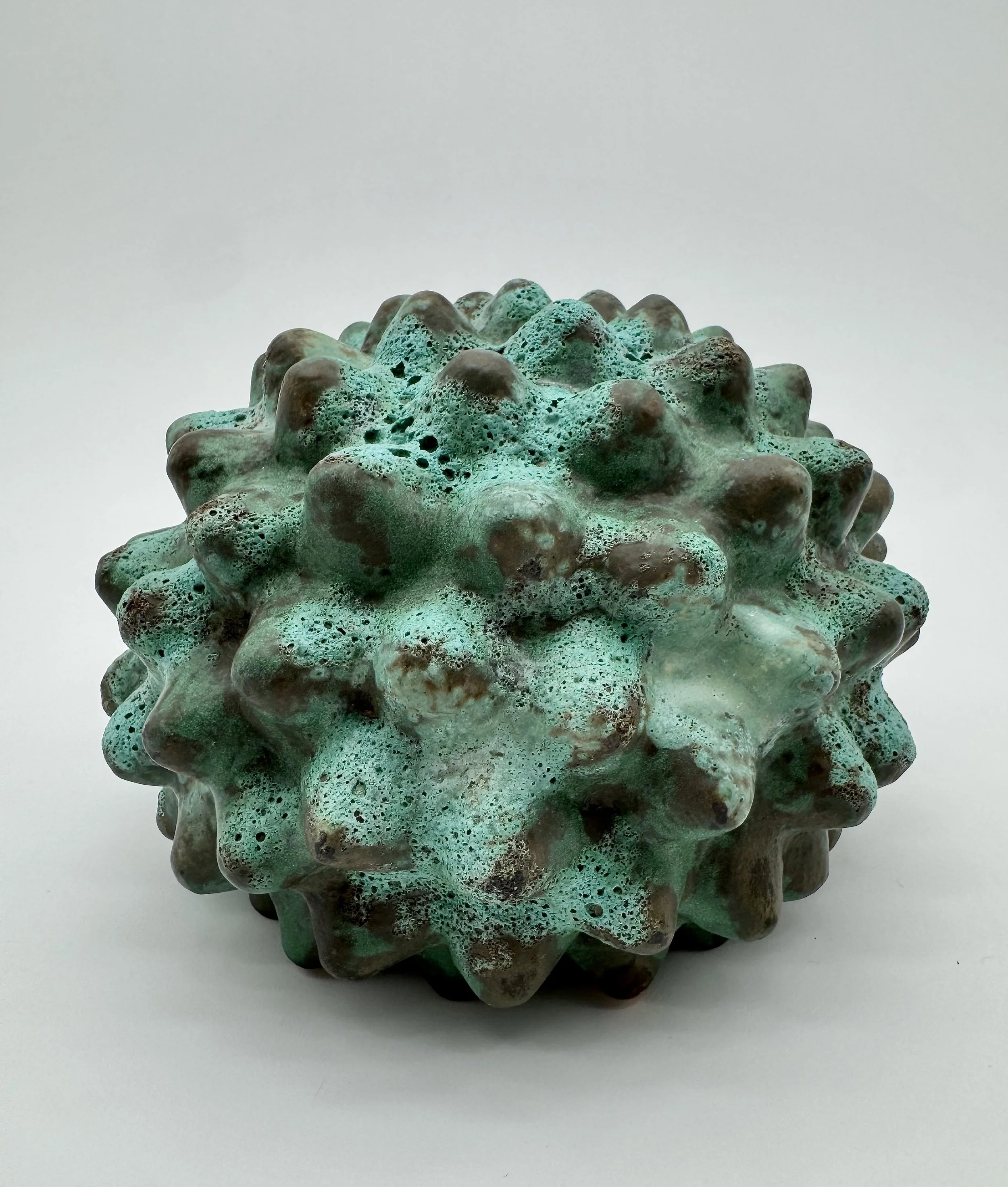 Close-up of a textured ceramic sculpture with a greenish-blue glaze, set against a plain white background.