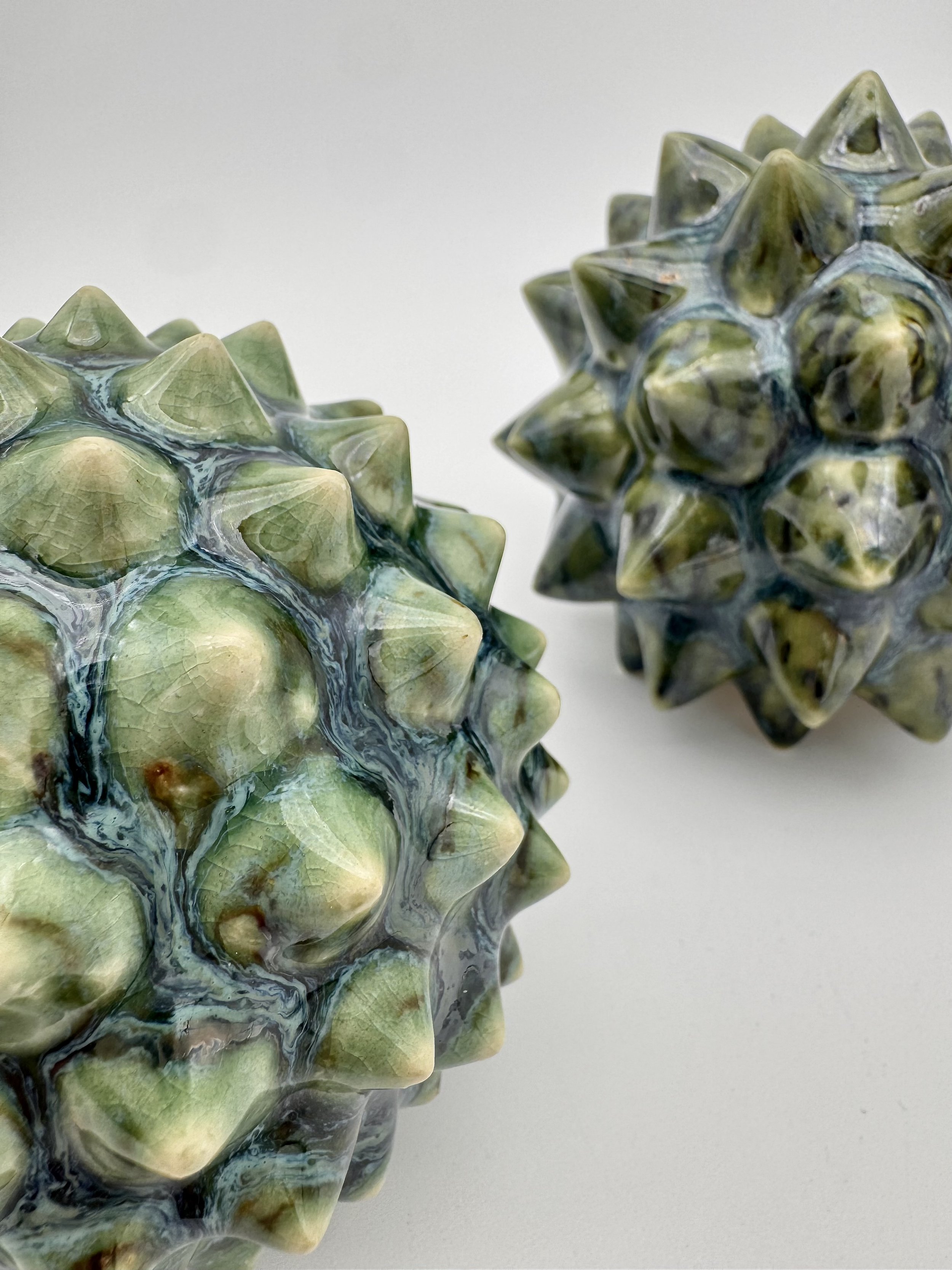 Close-up of two spiky, textured decorative objects with green and yellow hues on a plain white background.