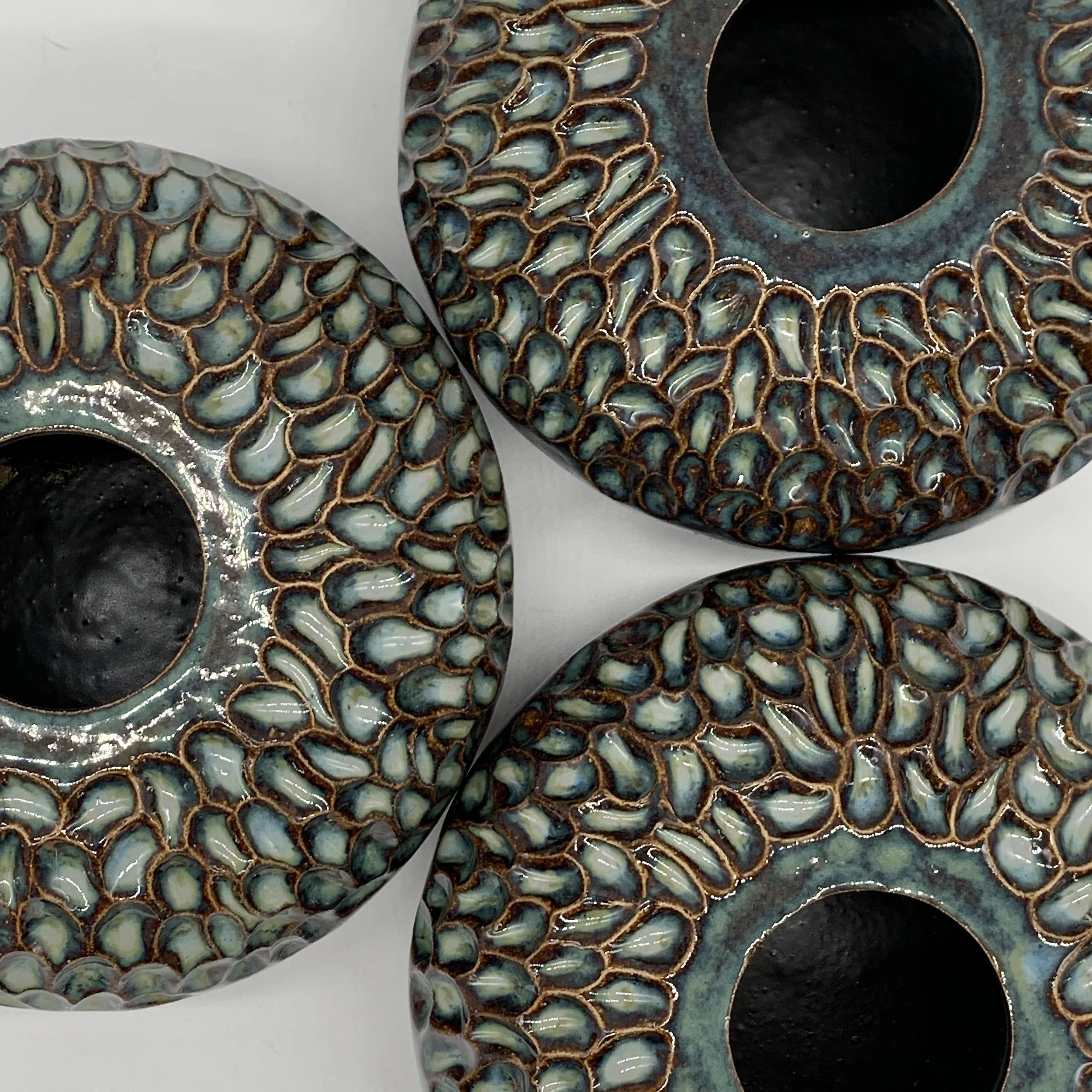 Close-up of a ceramic object with aquamarine-colored pebble-like glazed surface and brown outlining, with part of a white background visible.