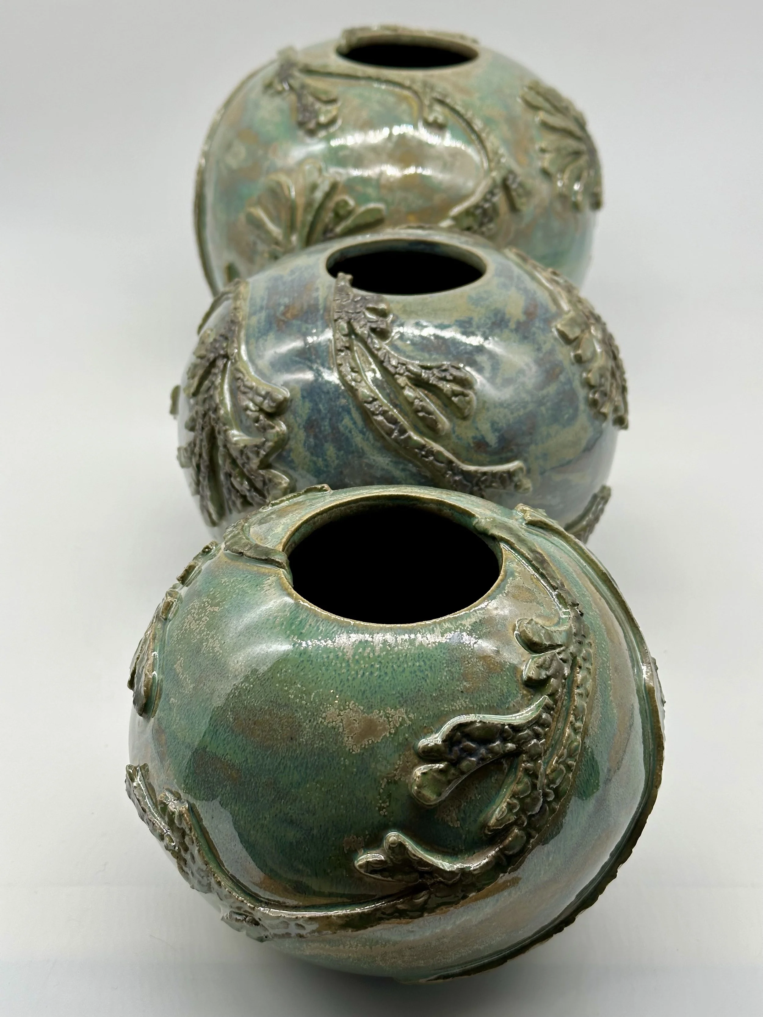Three decorative ceramic vases with raised floral and leaf patterns, arranged in a column on a white surface.