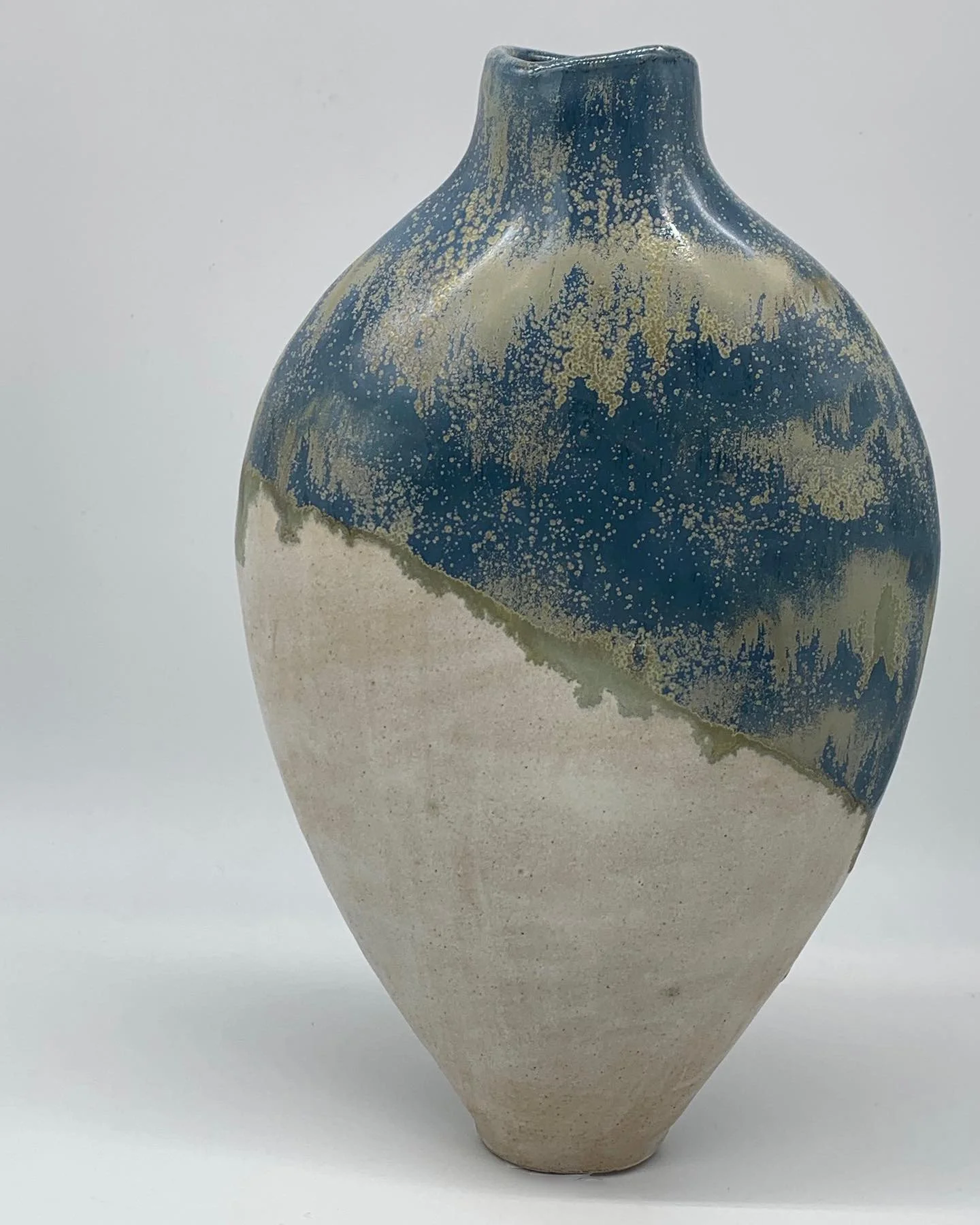 Ceramic vase with a sandy lower half and a darker, speckled blue top section, featuring a rounded body and narrow opening.