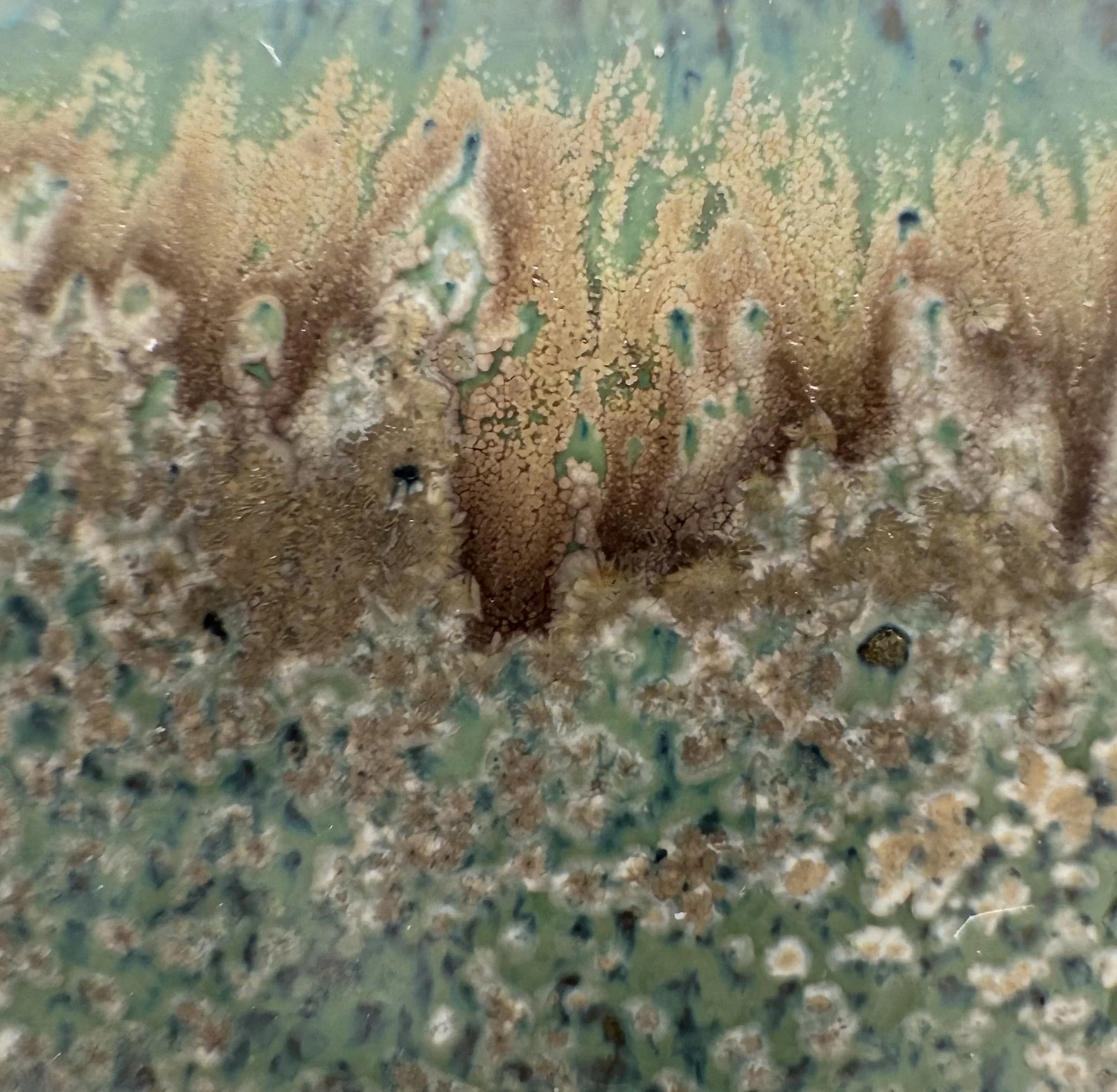 Close-up of a textured, multicolored surface with brown, green, and blue tones and small holes.