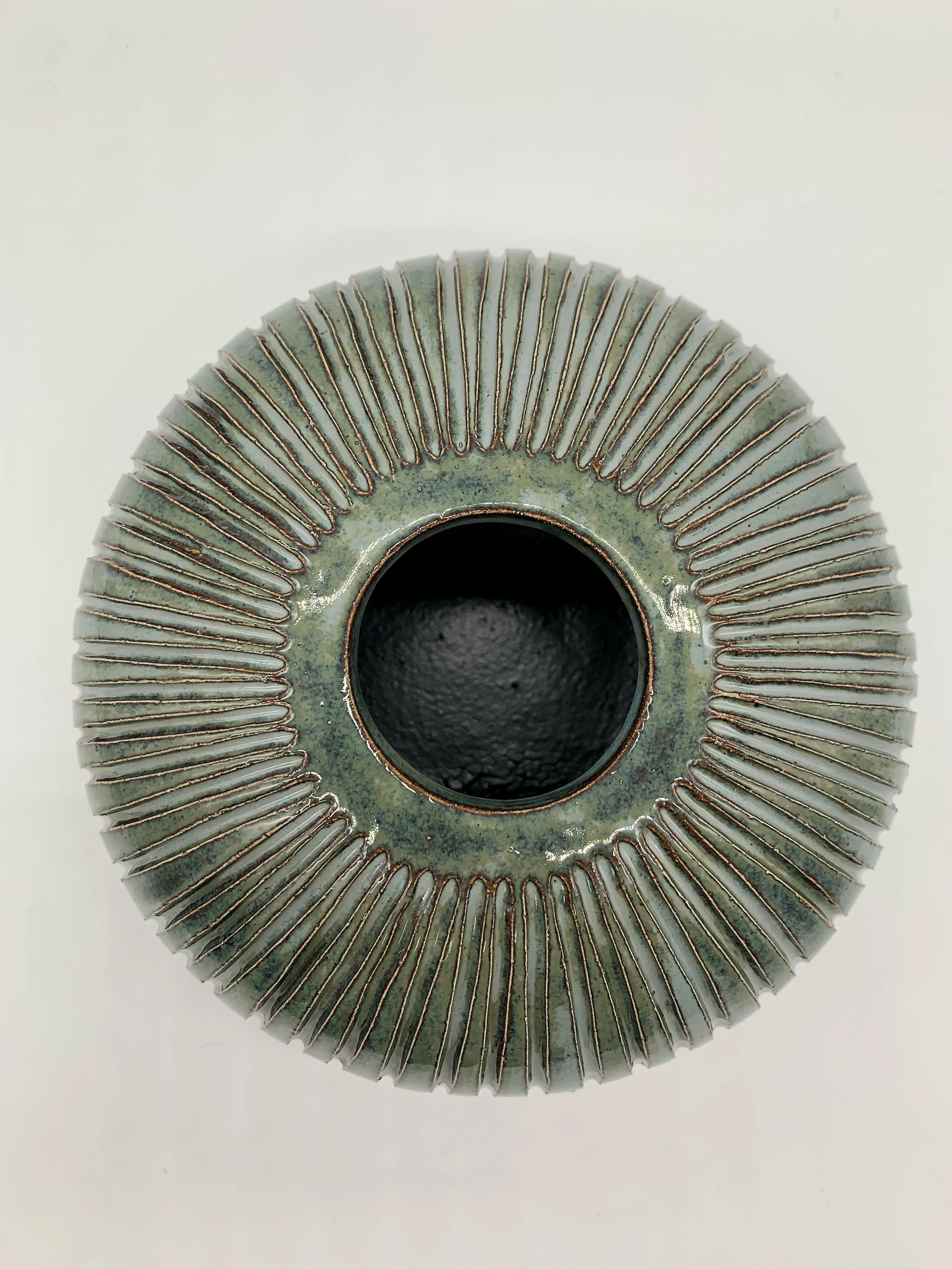Close-up of a decorative ceramic or metallic object with radiating lines and a central hole, on a white background.