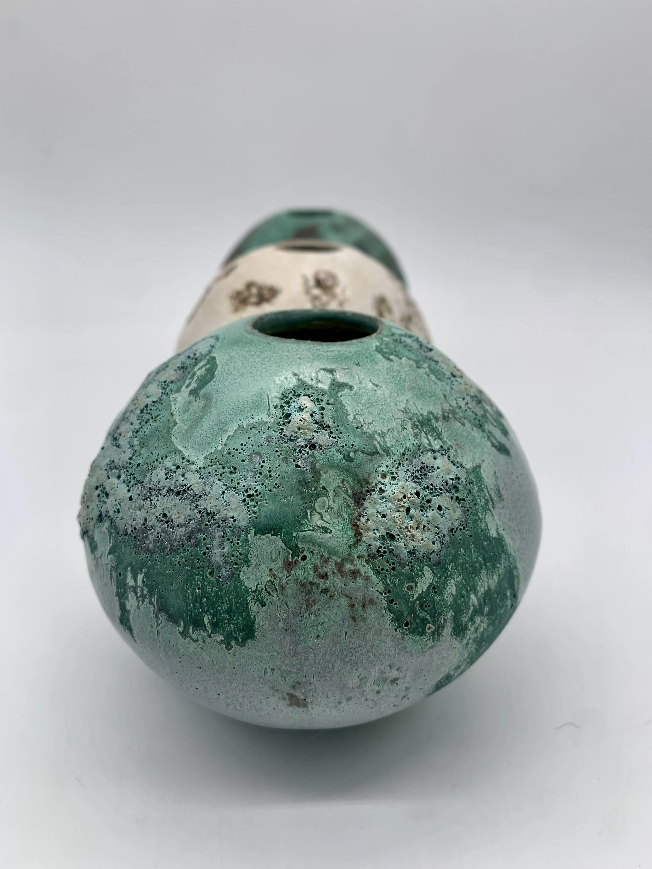 A collection of three ceramic vases in varying shades of green and white, with textured and glazed surfaces, arranged in a line on a white background.