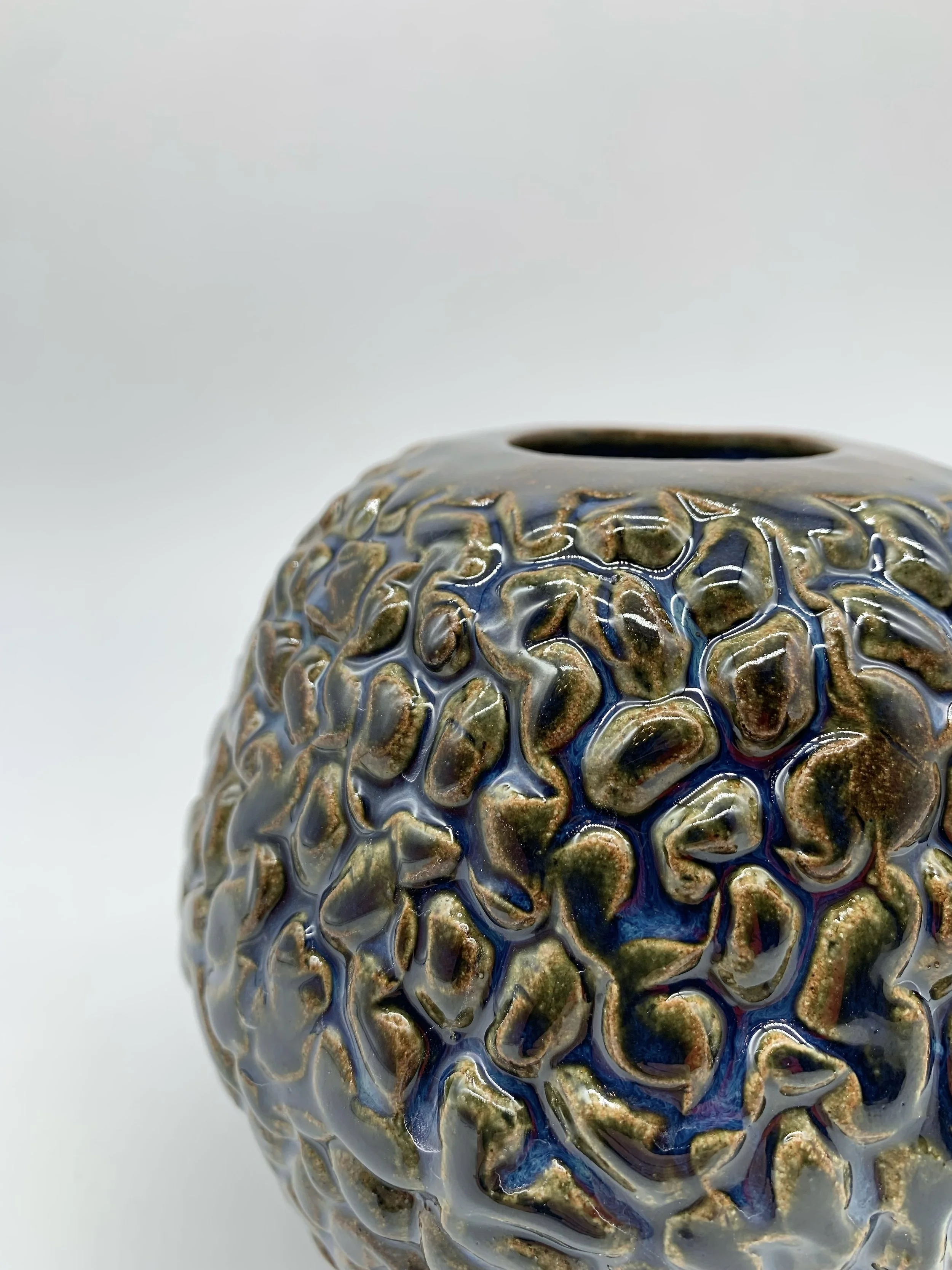 Close-up of a decorative ceramic vase with a textured, green and blue glazed surface on a white background.