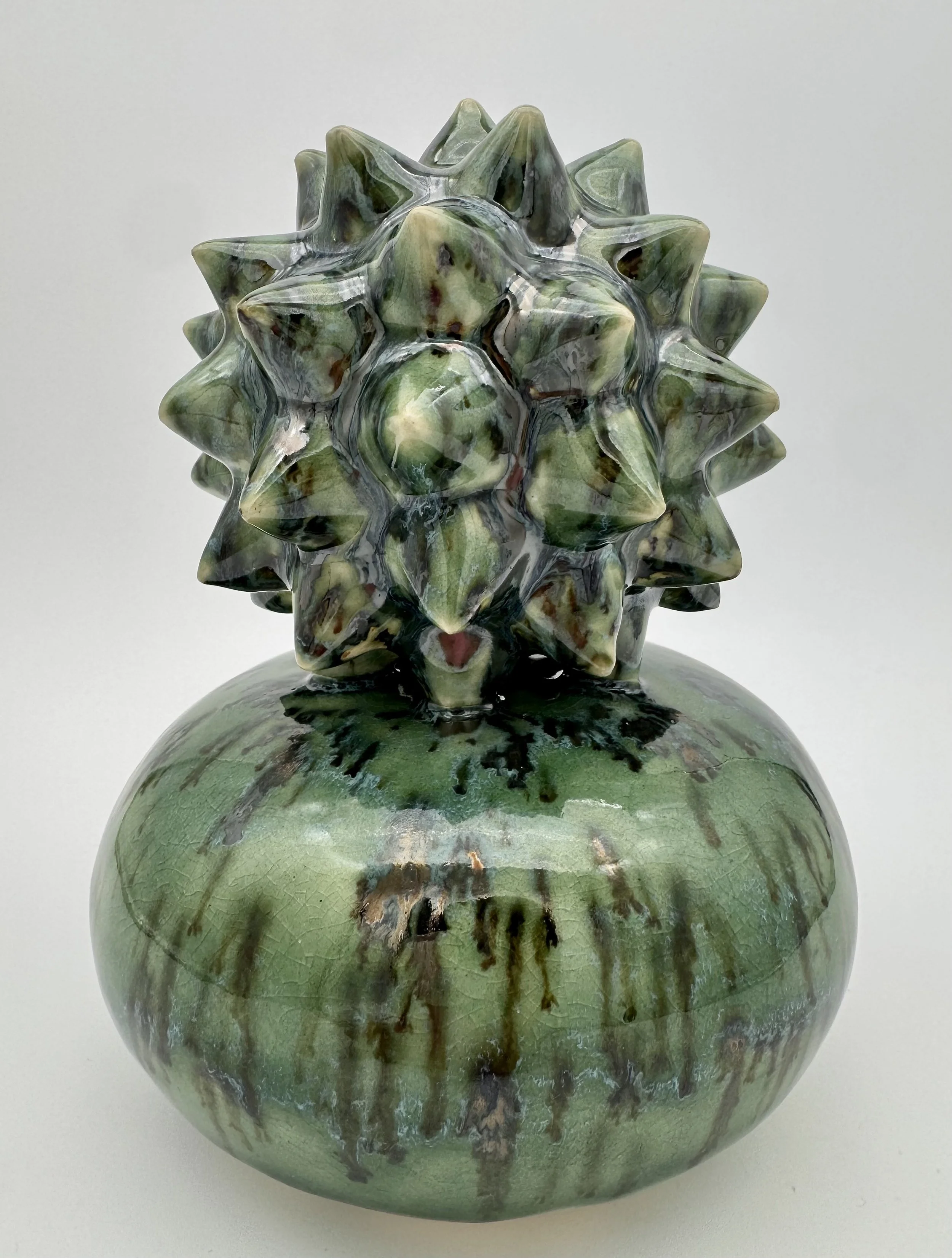 A decorative ceramic vase with a spherical shape, featuring a layered, textured, and glossy green surface with darker streaks and cracks.