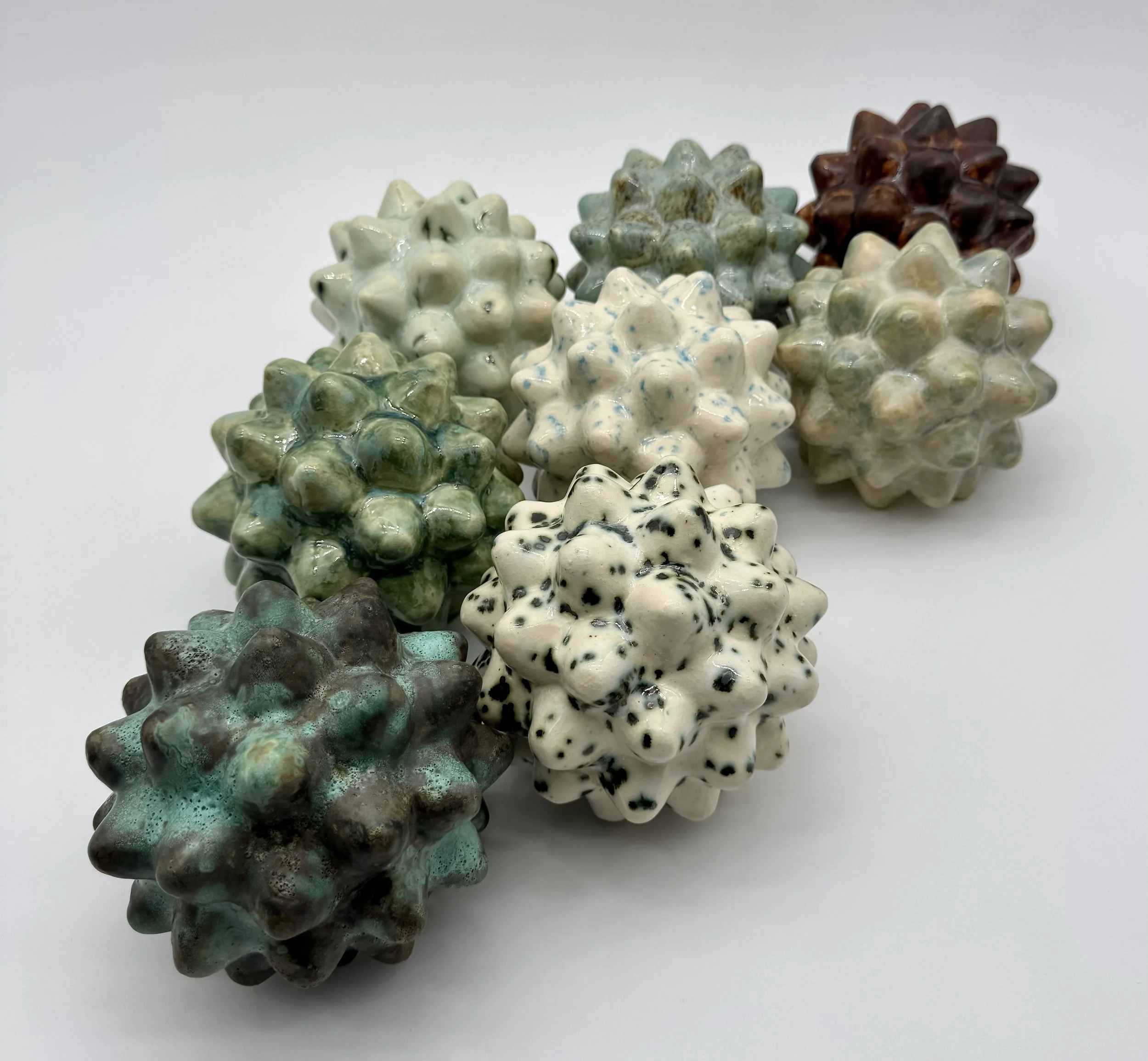 A group of ceramic star-shaped sculptures in various colors, including white, green, brown, and black, arranged against a plain white background.