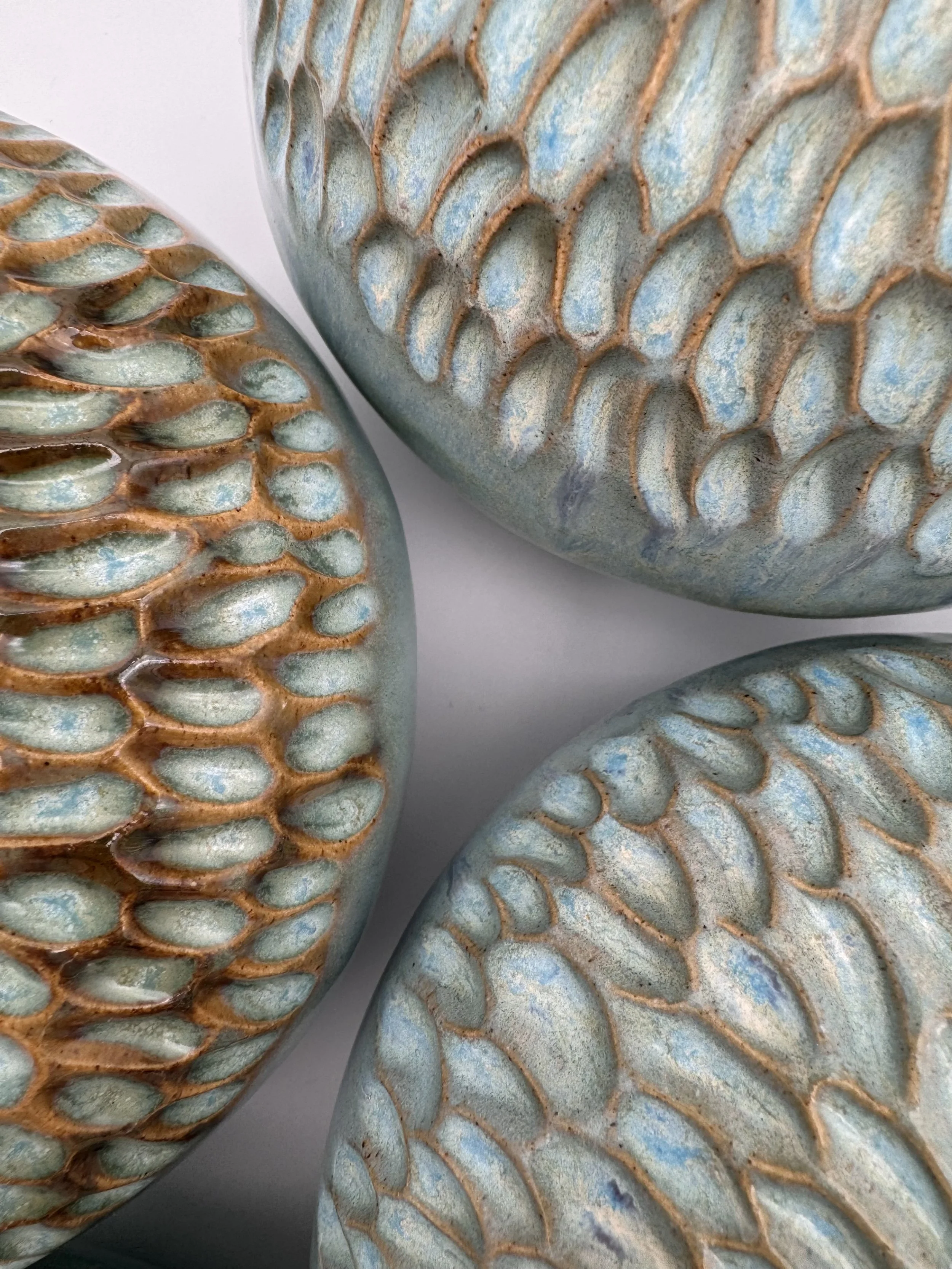 Close-up of textured ceramic vases with a light greenish-blue glaze, featuring raised, irregular, net-like patterns outlined in brown.