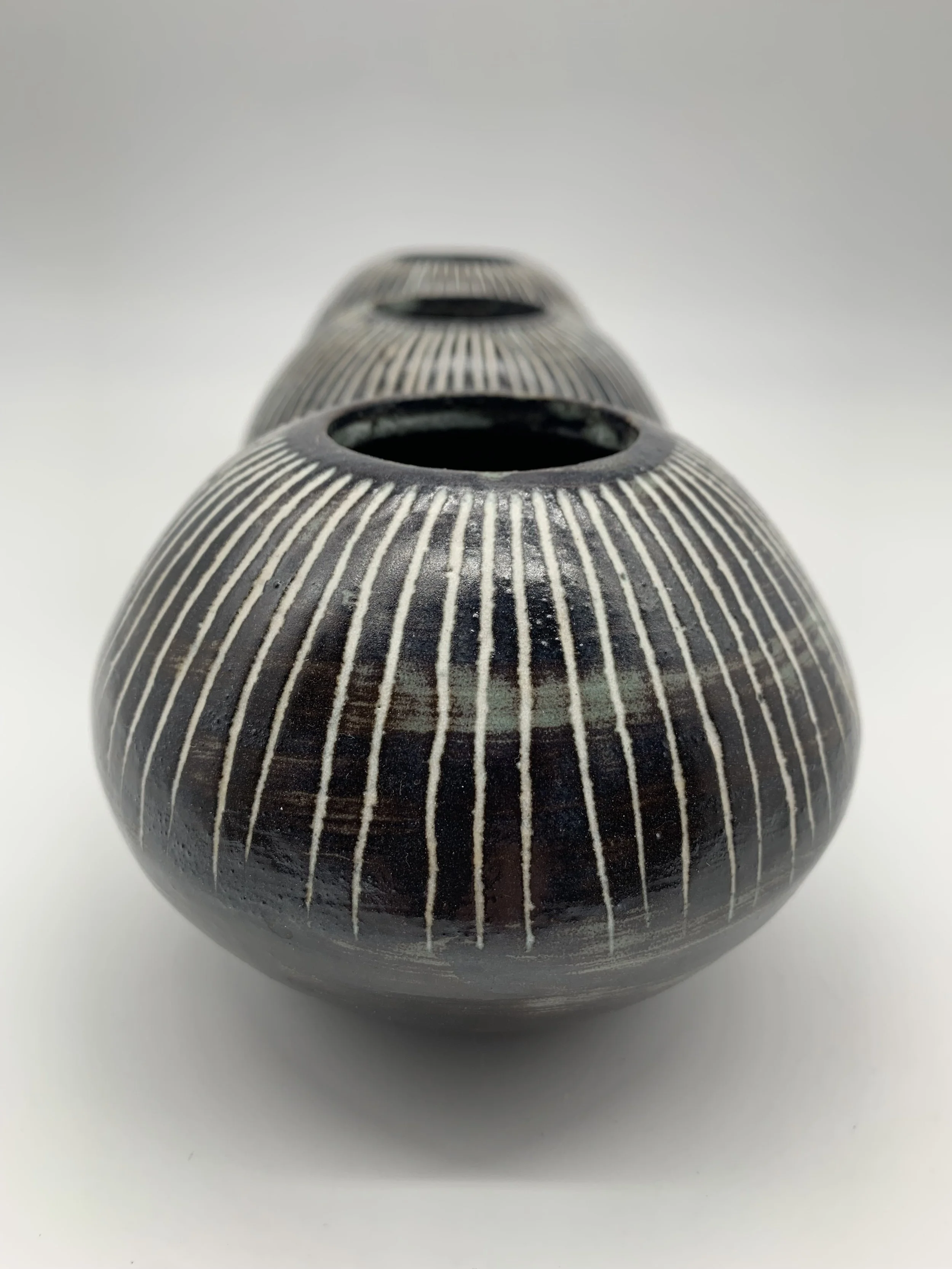 Black and white ceramic vase with vertical striped pattern and circular openings at the top, placed on a white surface.