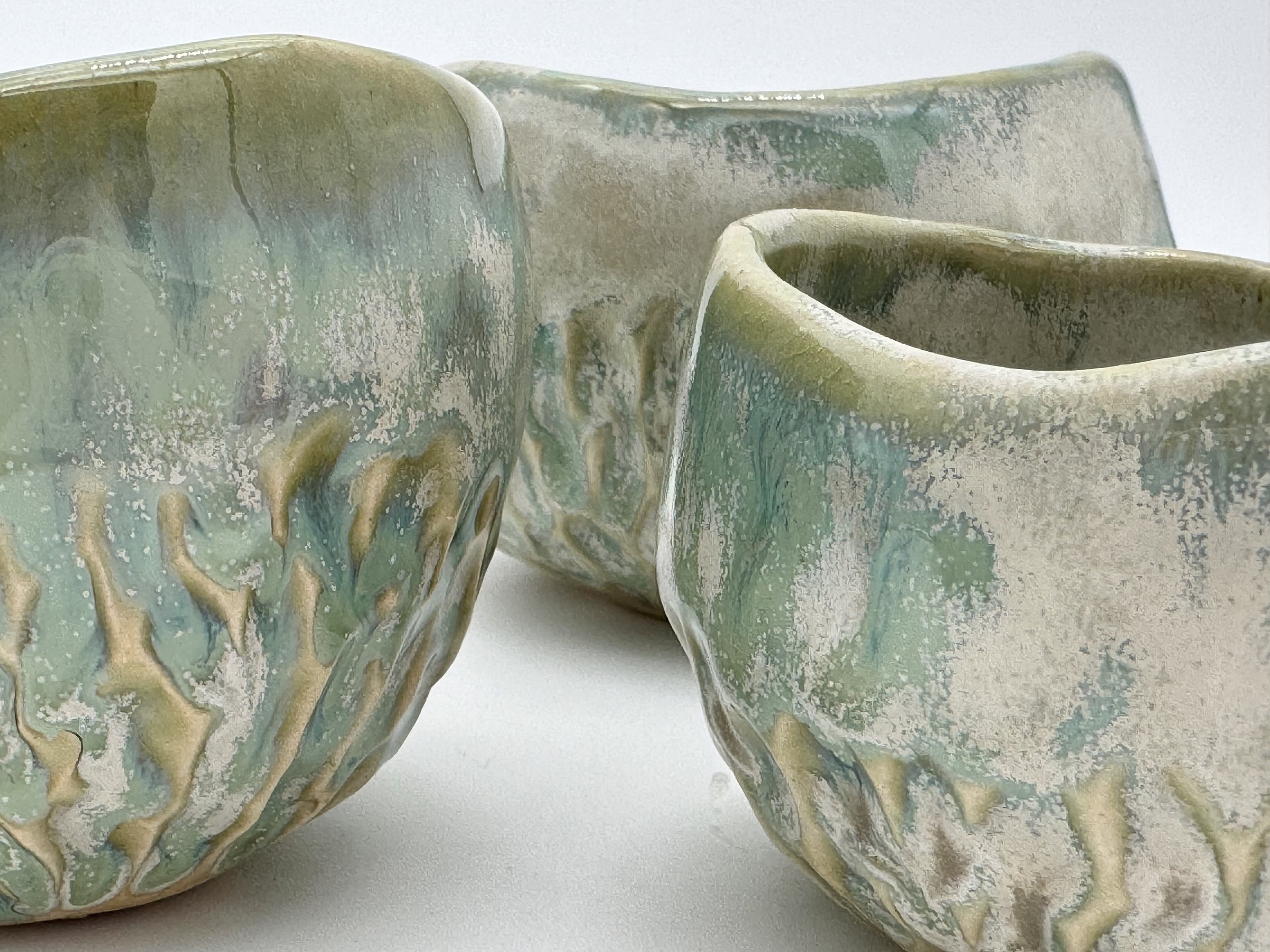 Close-up of a ceramic mug with a textured surface, glazed in shades of green, blue, and beige with a drip glaze design.