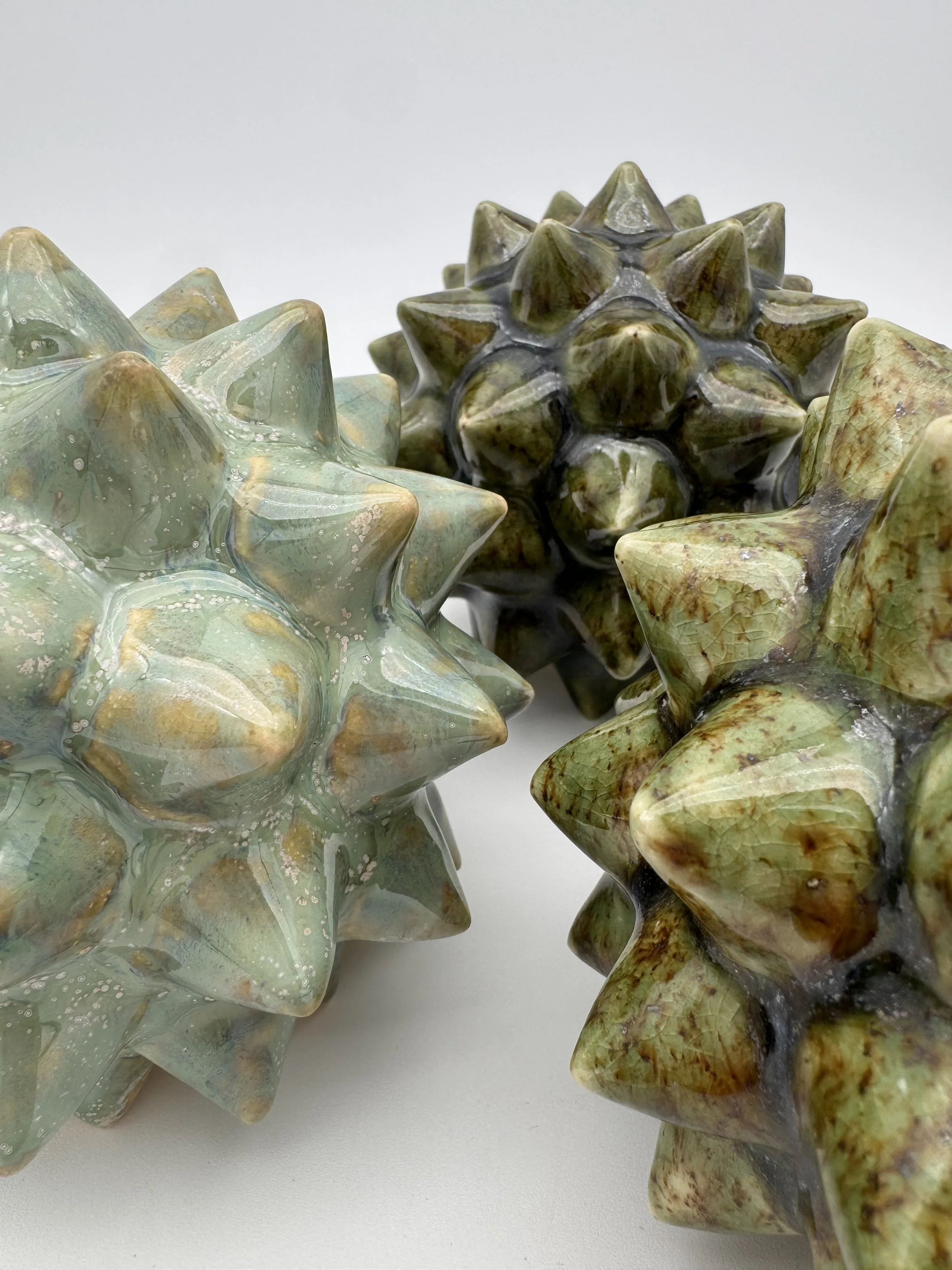 Close-up view of two decorative glass star-shaped sculptures with spiked surfaces, one greenish and the other brownish, set against a plain white background.