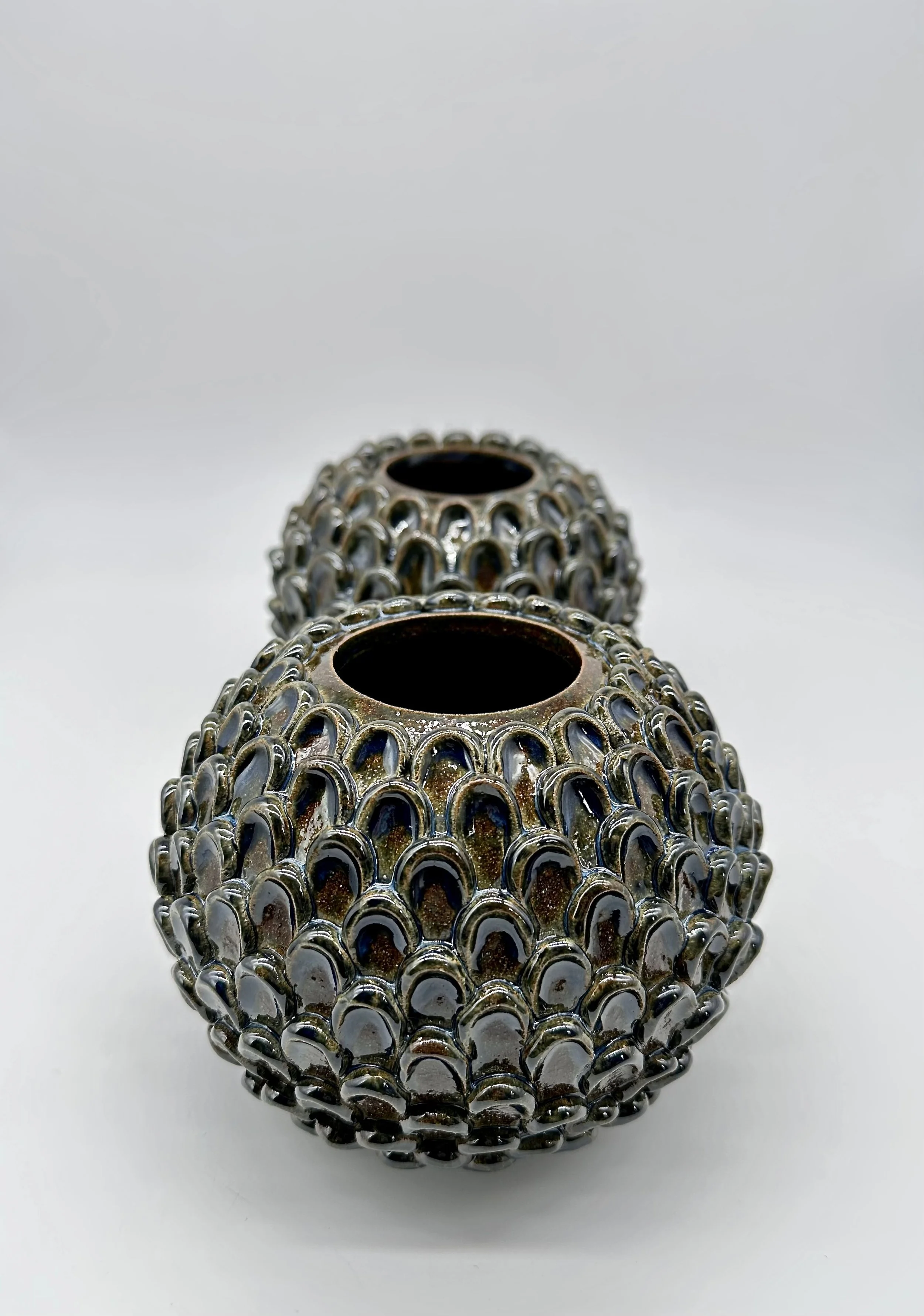 Three decorative metal vases with open tops, covered in an overlapping scale-like pattern, arranged on a white surface.