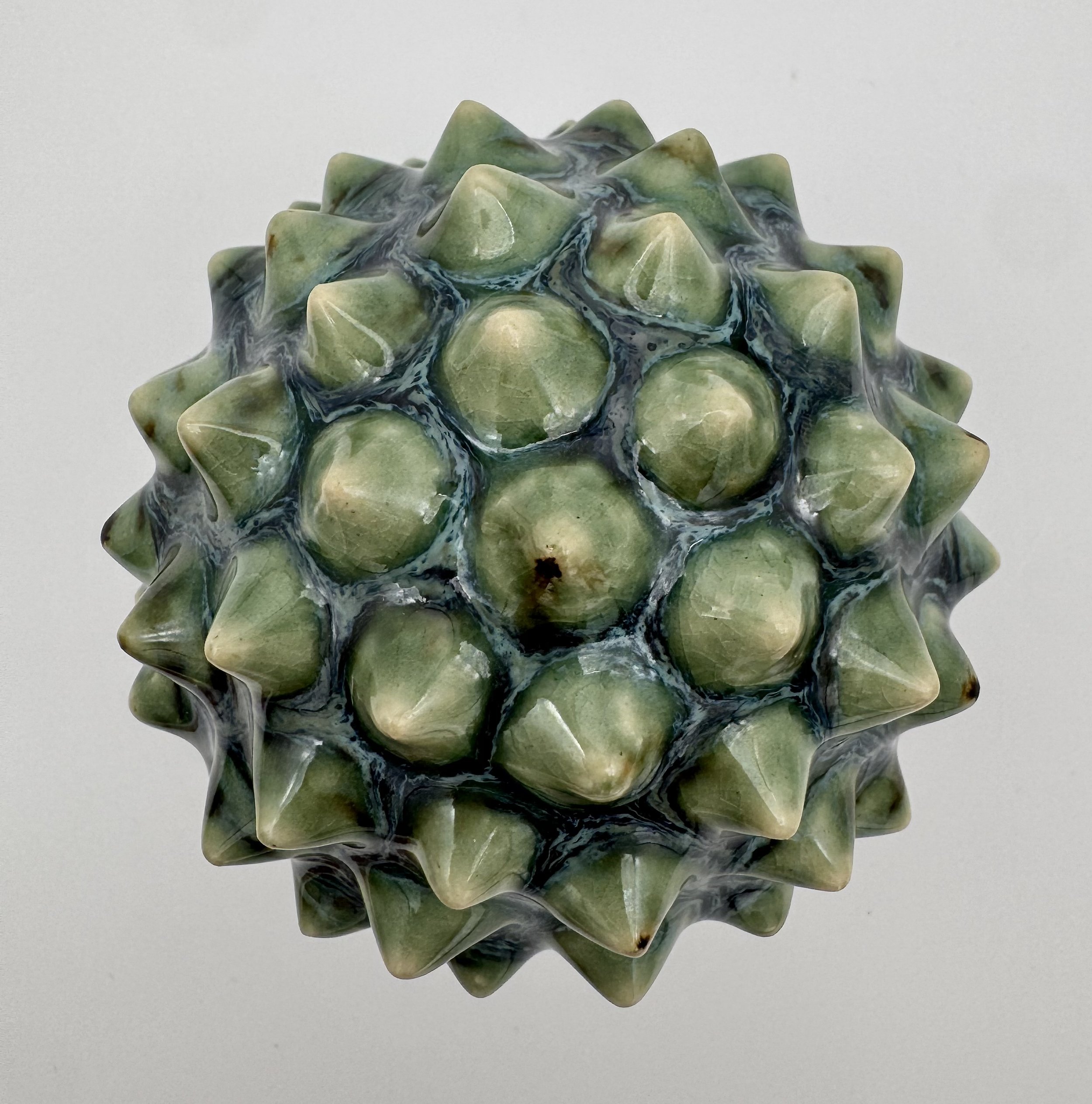 Close-up of a ceramic or glass decorative object resembling a sea urchin with a glossy, marbled green and black pattern.