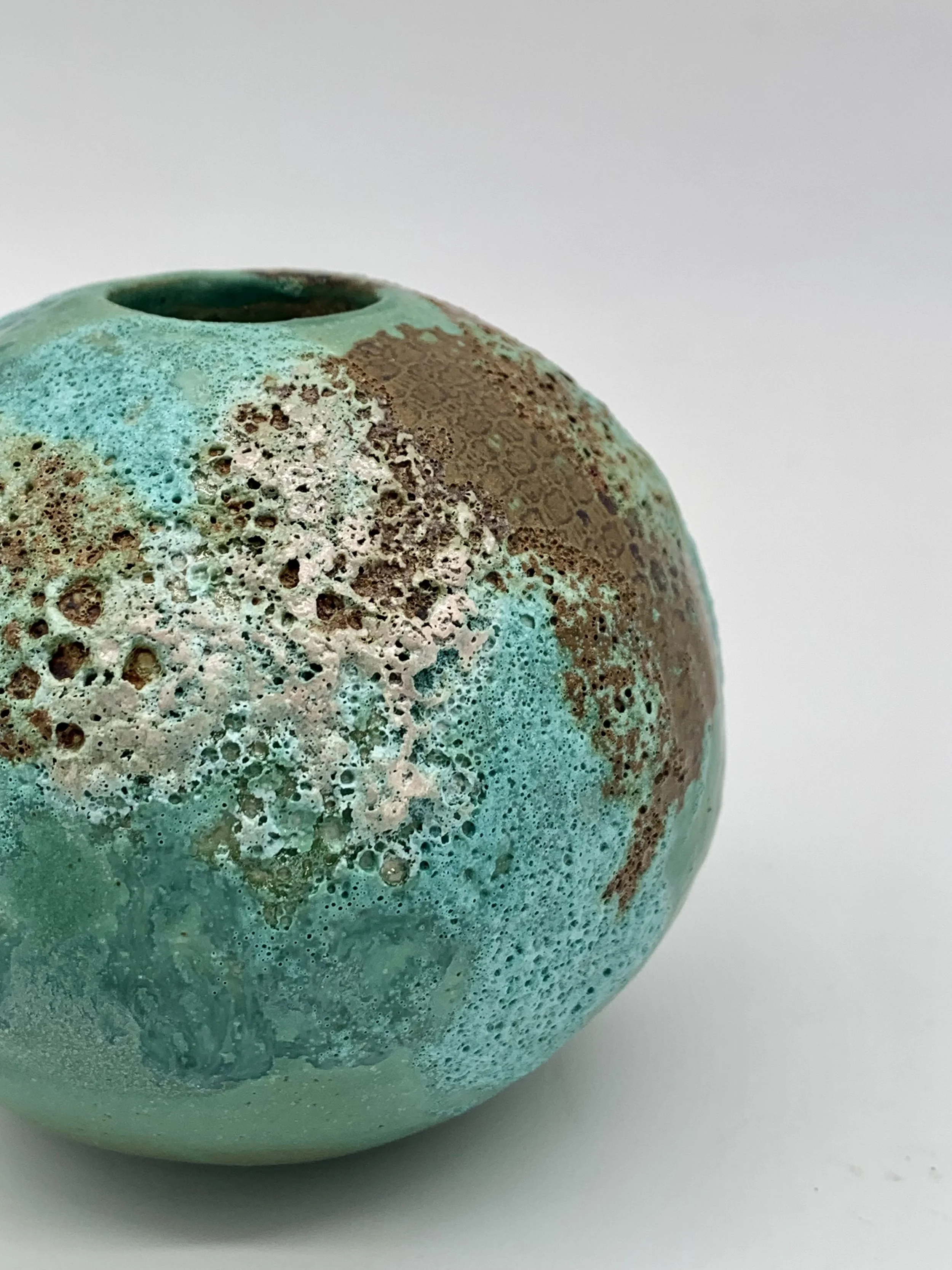Close-up of a textured ceramic vase with a turquoise and brown glaze on a white surface.
