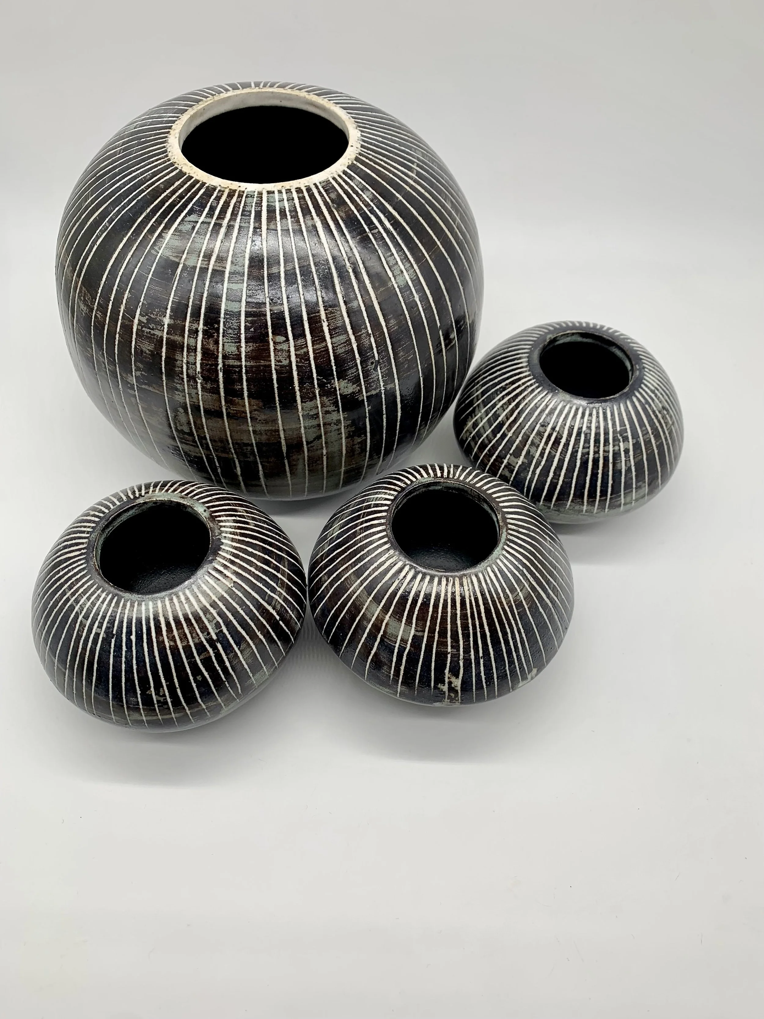 Four round, black ceramic vases with white striped patterns on a white background.