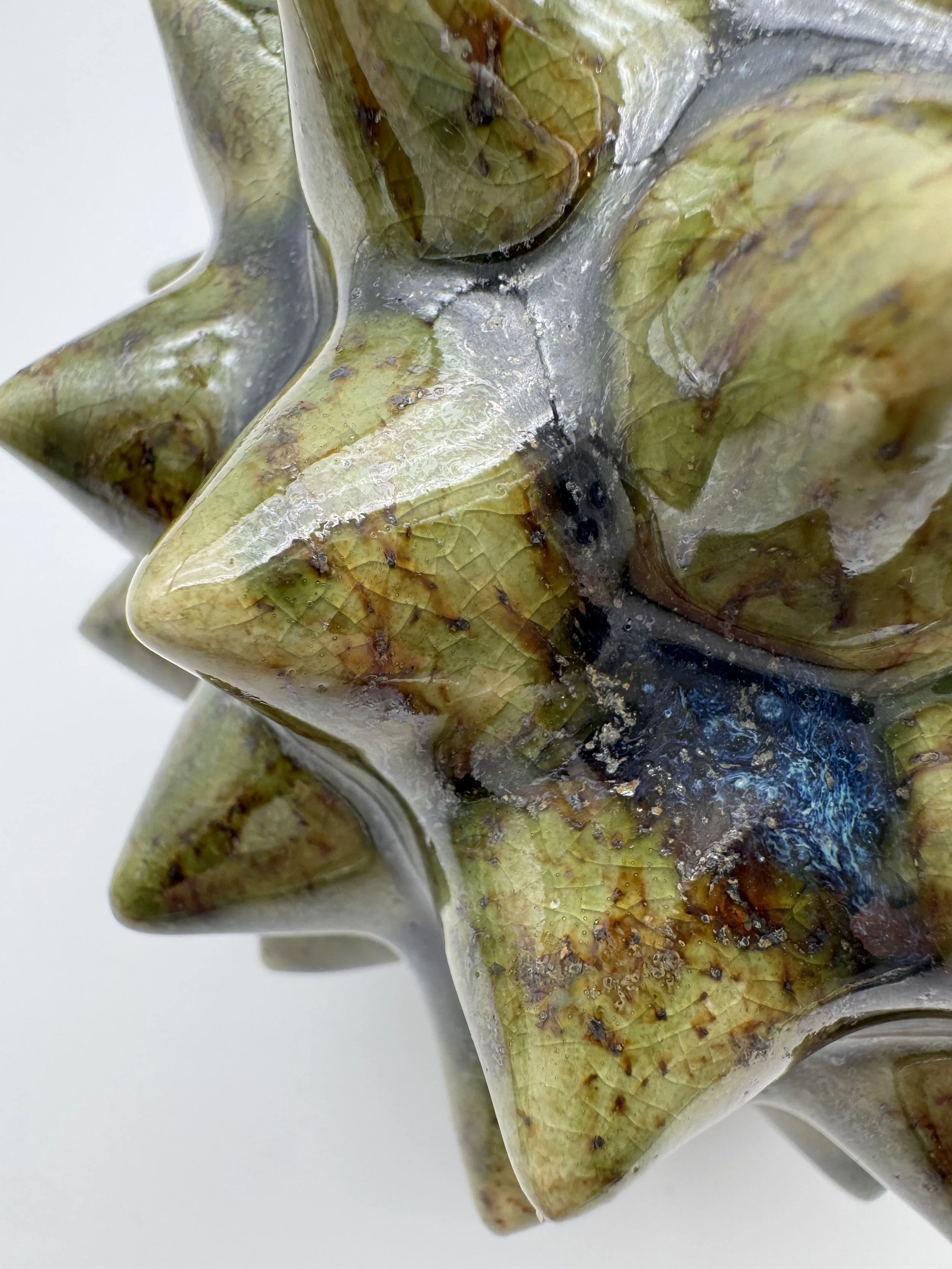 Close-up of a burnt and weathered sculpture with gold and greenish hues and cracks, showing a textured surface.