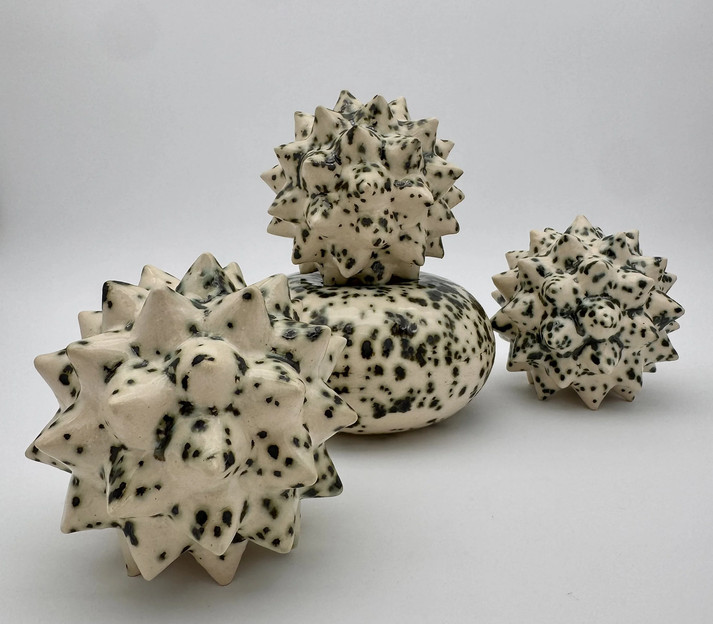 Close-up of multiple star-shaped ceramic objects with black speckles, arranged on a white surface with a plain light gray background.