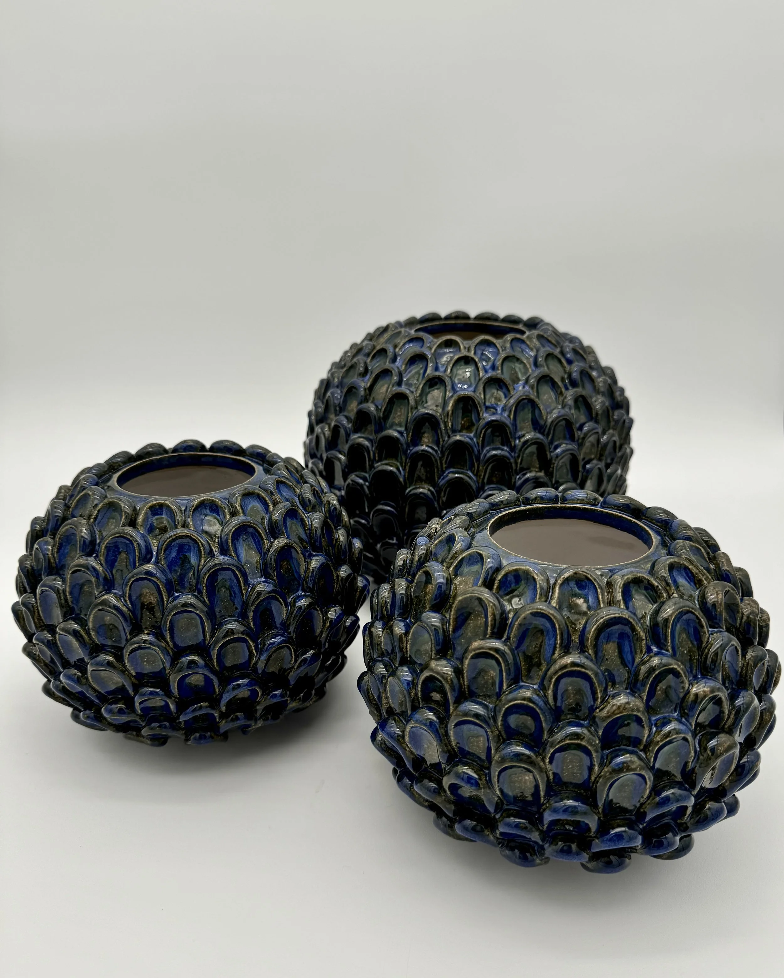 Three decorative glass vases with intricate blue and black patterns on a white surface against a plain gray background.