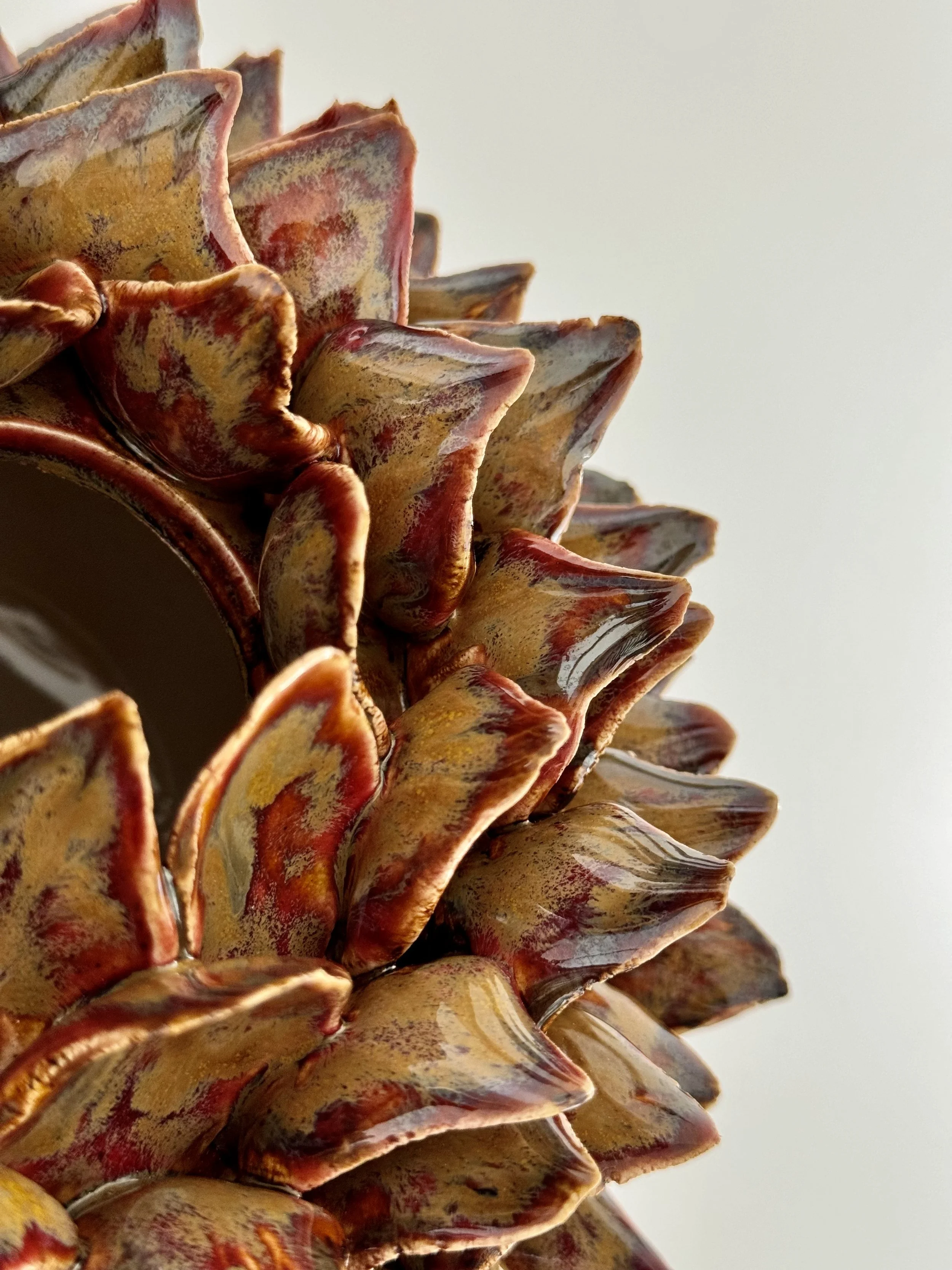 Close-up of a ceramic pinecone sculpture with a multicolored, textured surface featuring shades of red, yellow, and brown.