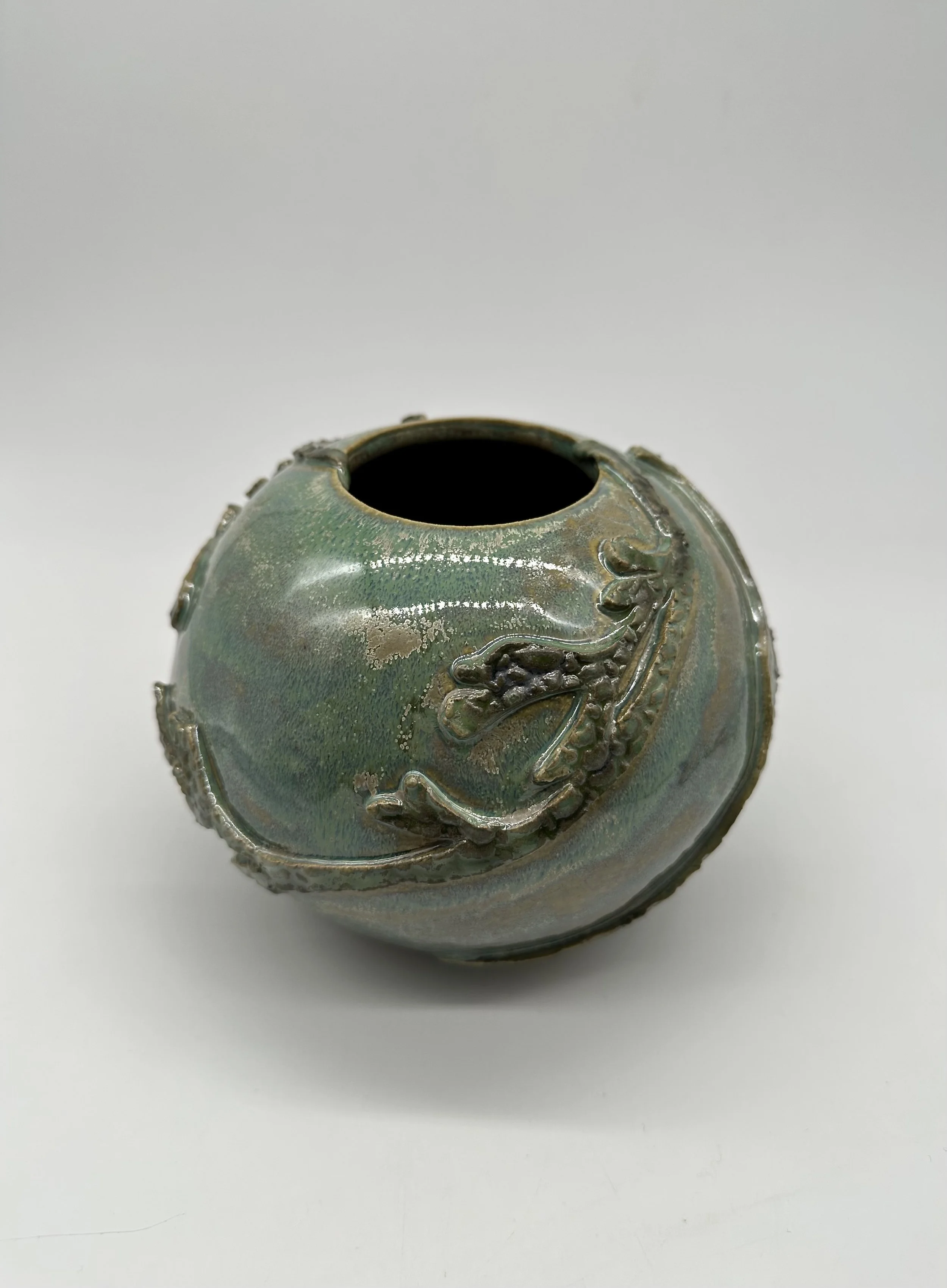 A ceramic vase with a textured surface and a dragon design in greenish glaze, viewed from the top against a white background.