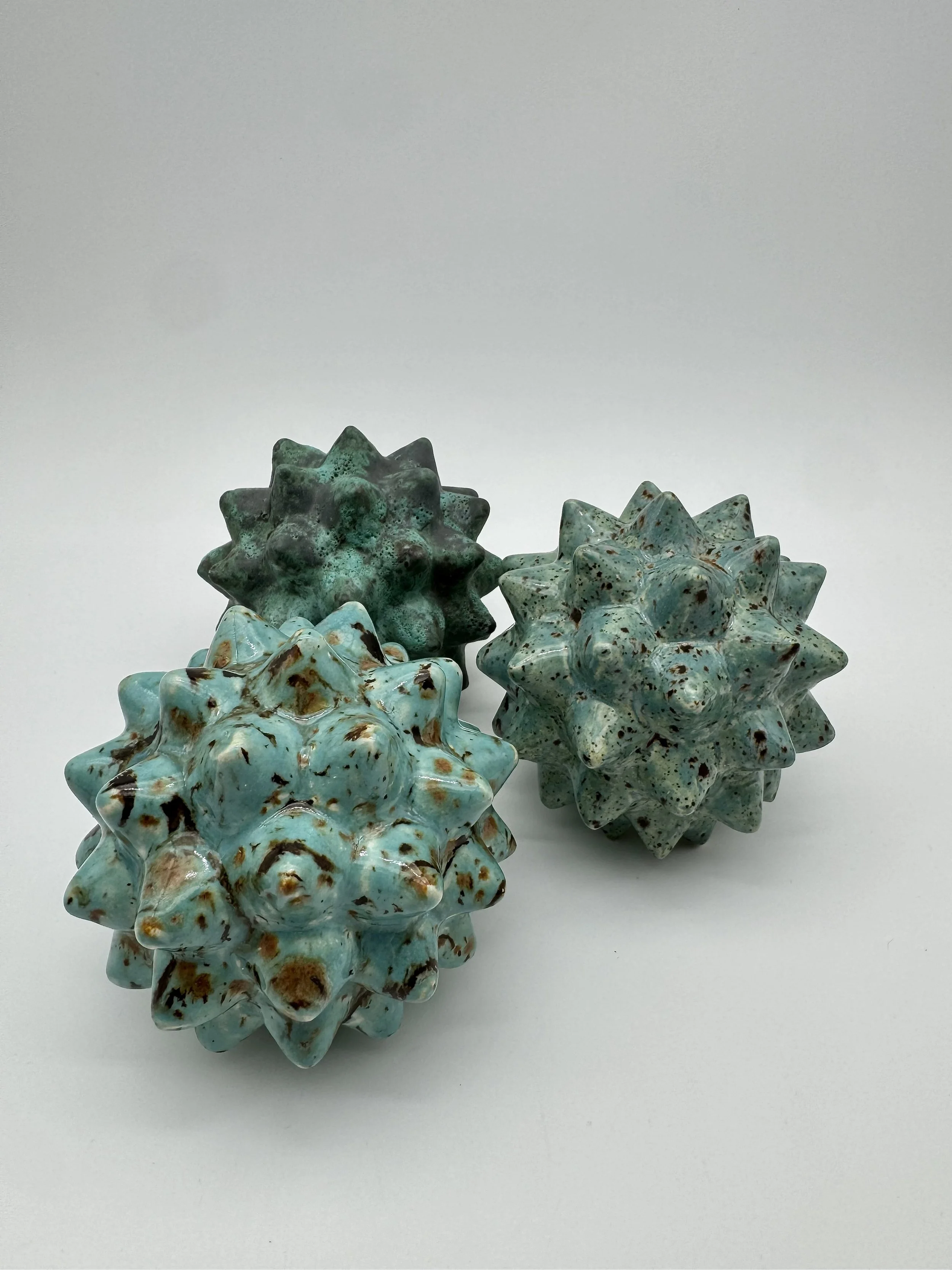 Three star-shaped ceramic objects with speckled turquoise glaze, placed on a white surface.