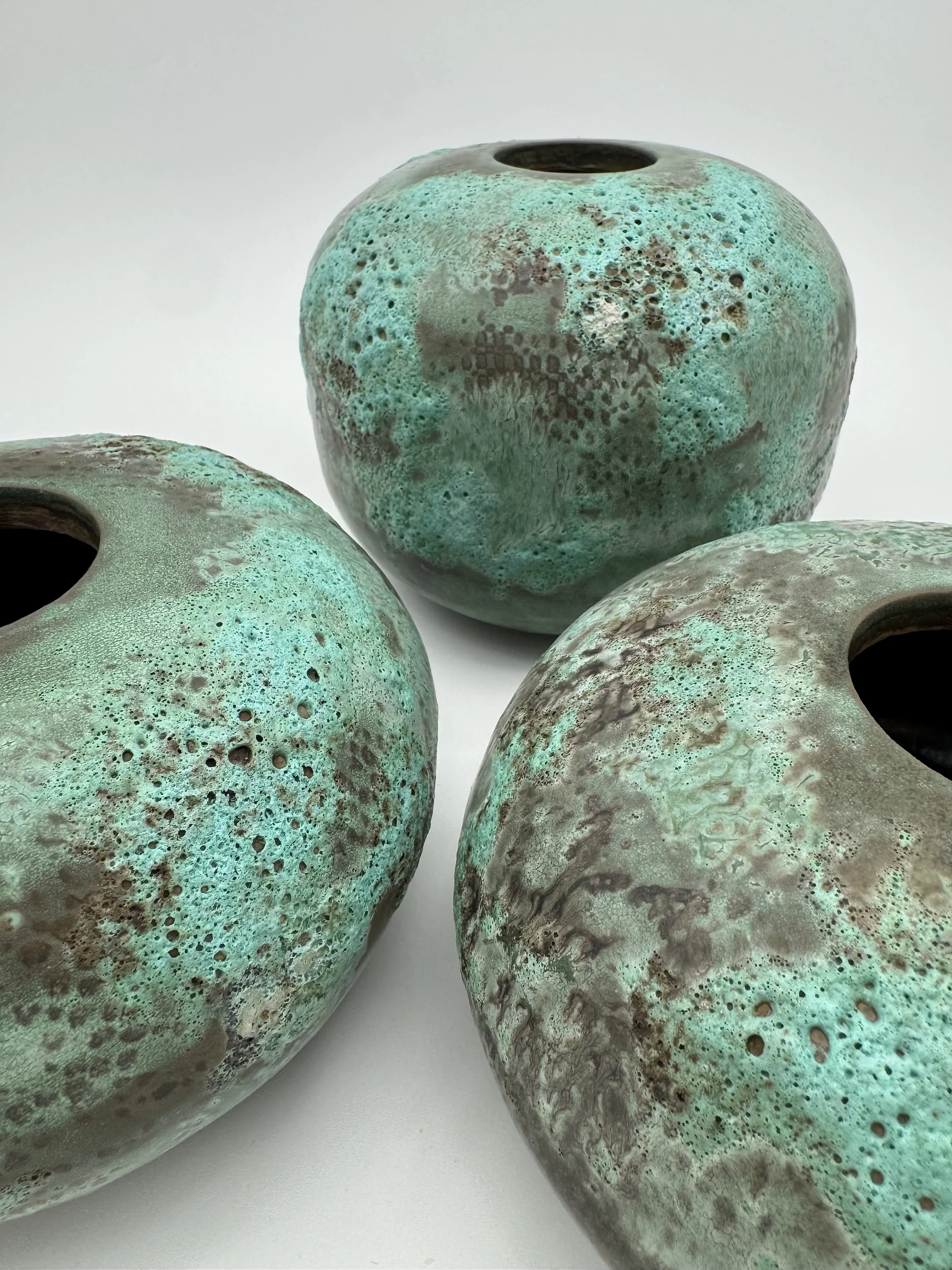 Close-up of four ceramic vases with green and brown marbled glaze on a white surface.