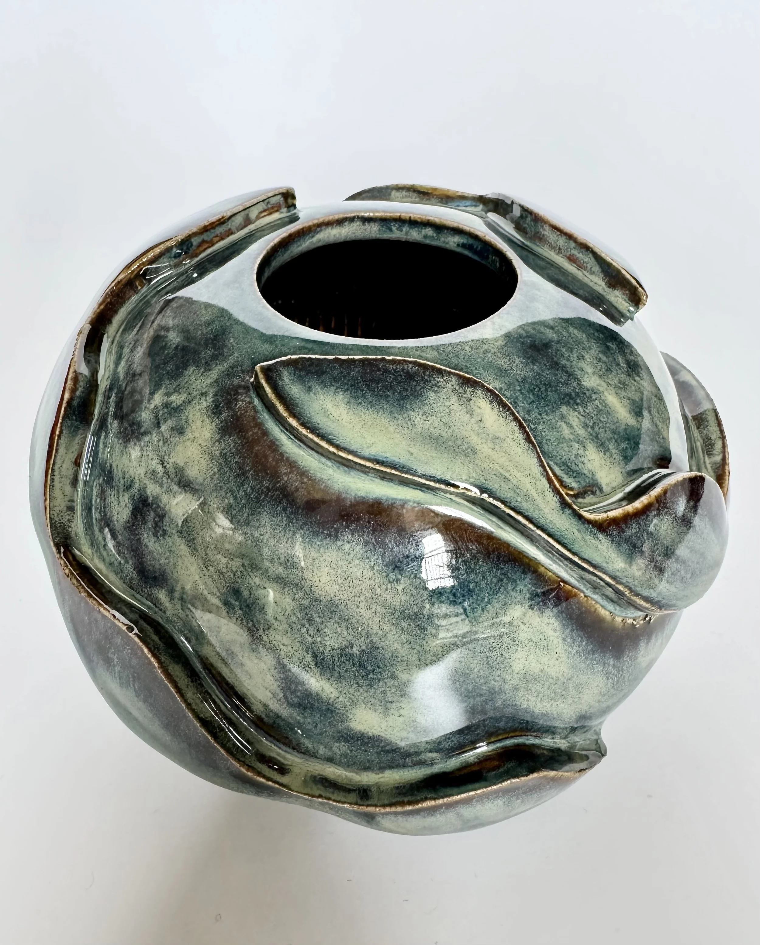 Close-up of a ceramic teapot with a swirl pattern and a dark opening, placed on a white surface.