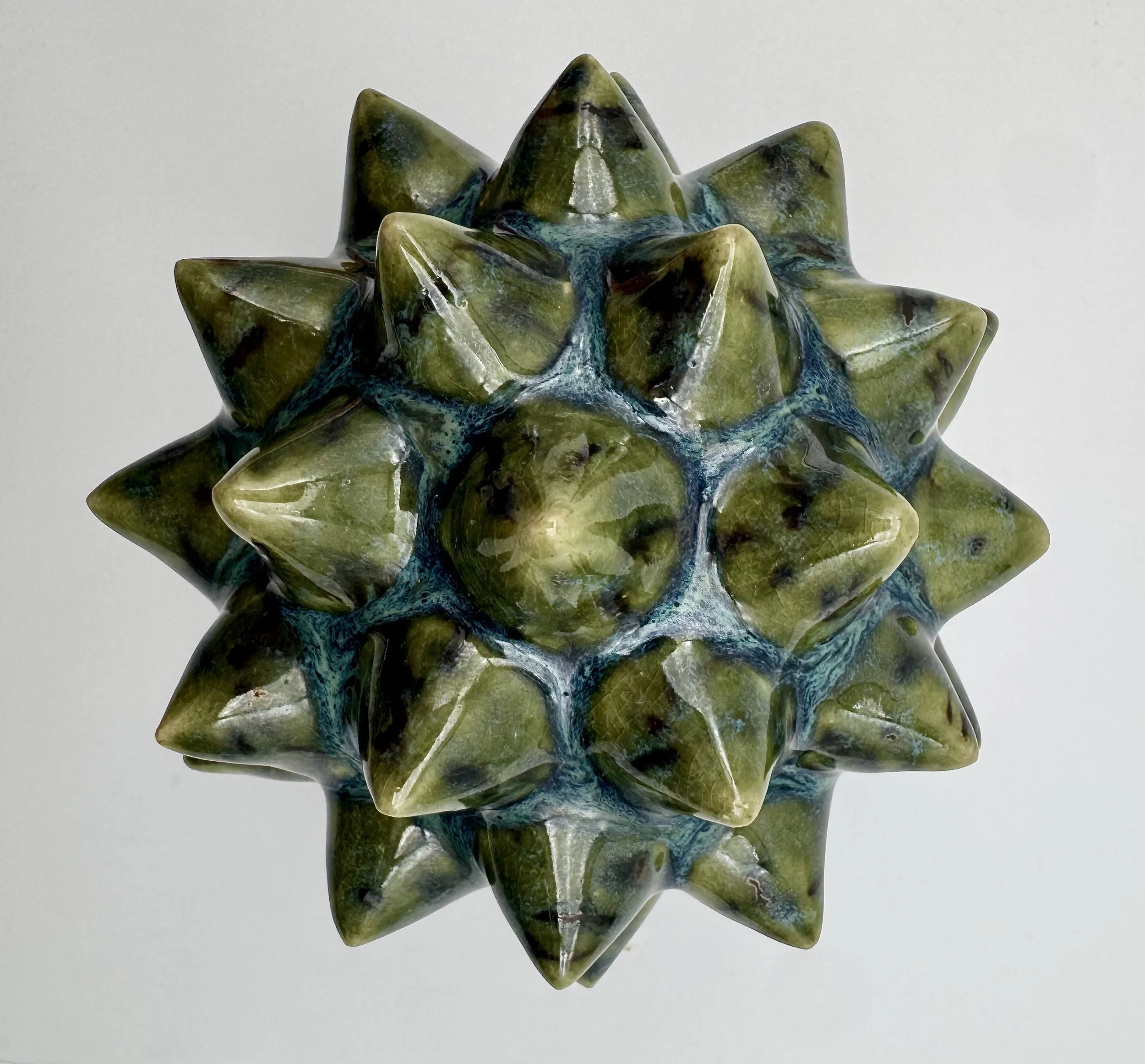 A green multicolored glass sculpture with spikes, resembling a lotus flower, reflected on a shiny surface.