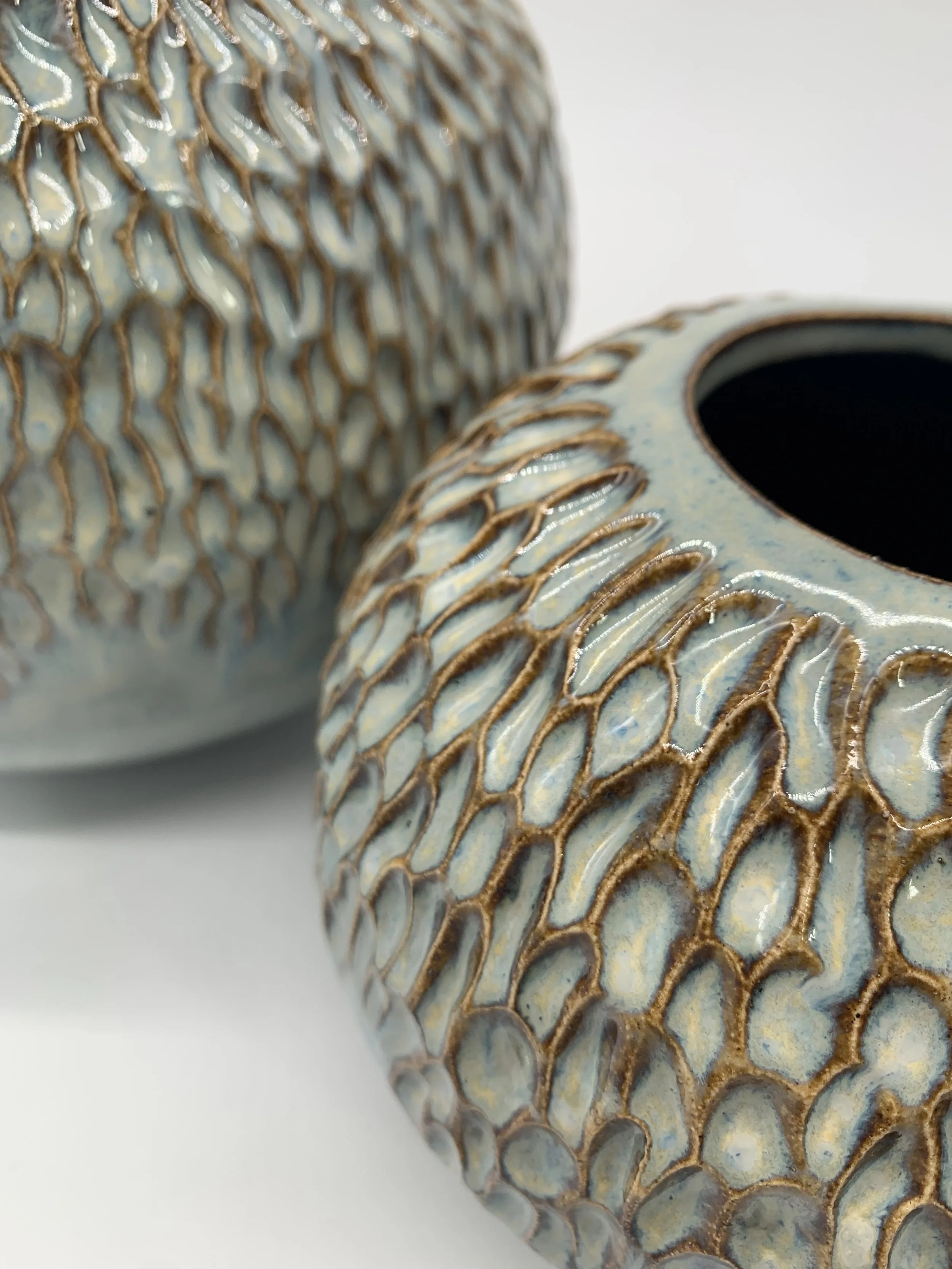 Close-up of a decorative ceramic object with textured, gold-embellished, honeycomb-like pattern on a light blue background.
