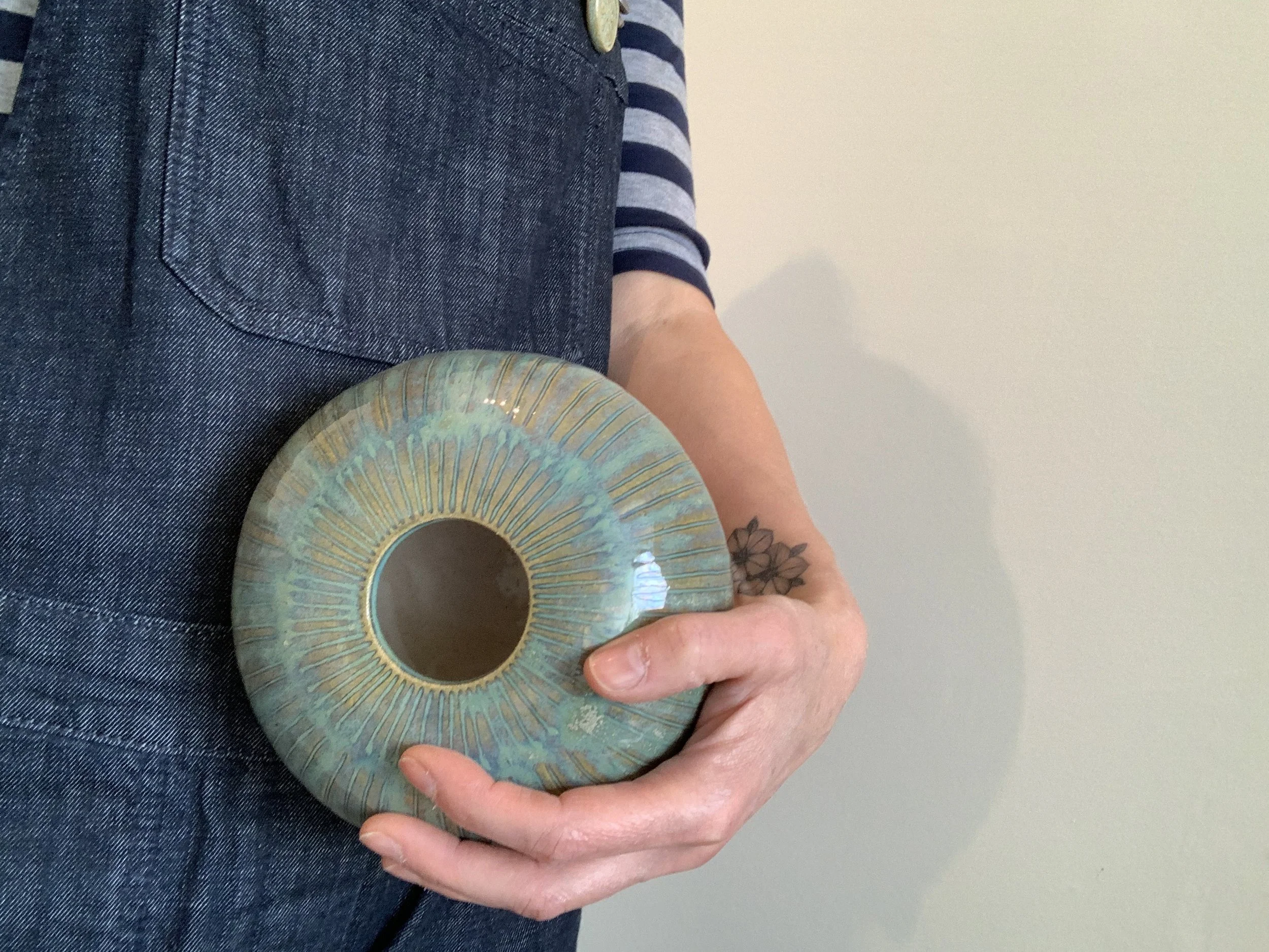 Person holding a decorative, circular ceramic dish with a radial pattern in shades of blue and yellow, wearing a dark striped shirt and jeans.