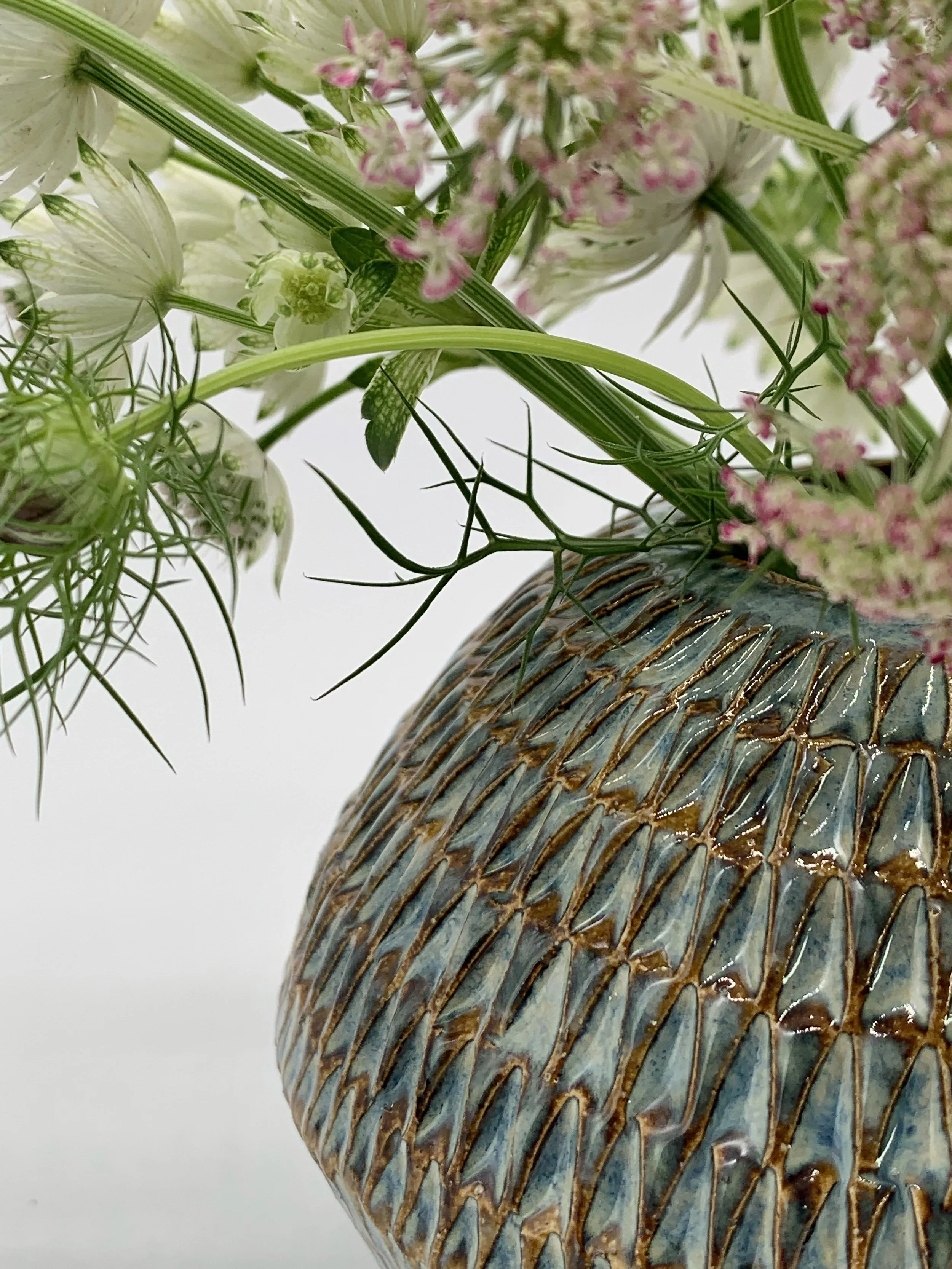 Close-up of a ceramic vase filled with various green and pink flowers and foliage, with a white background.