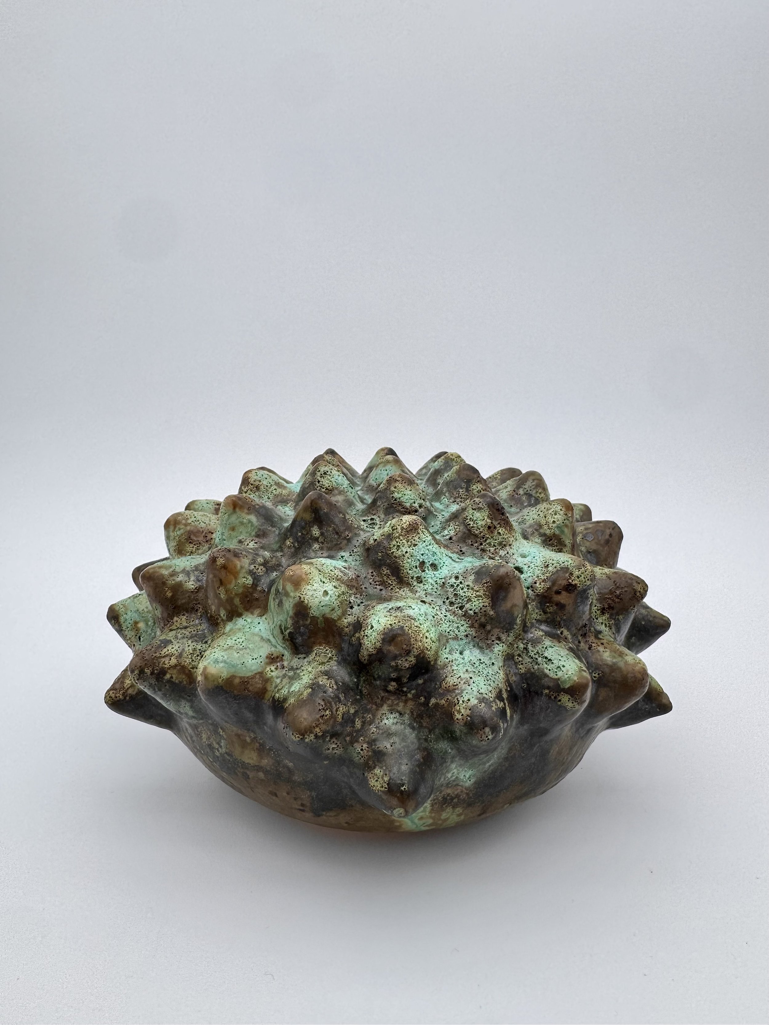 A decorative ceramic bowl with a textured, spiky surface and a glazed finish, placed on a plain white background.