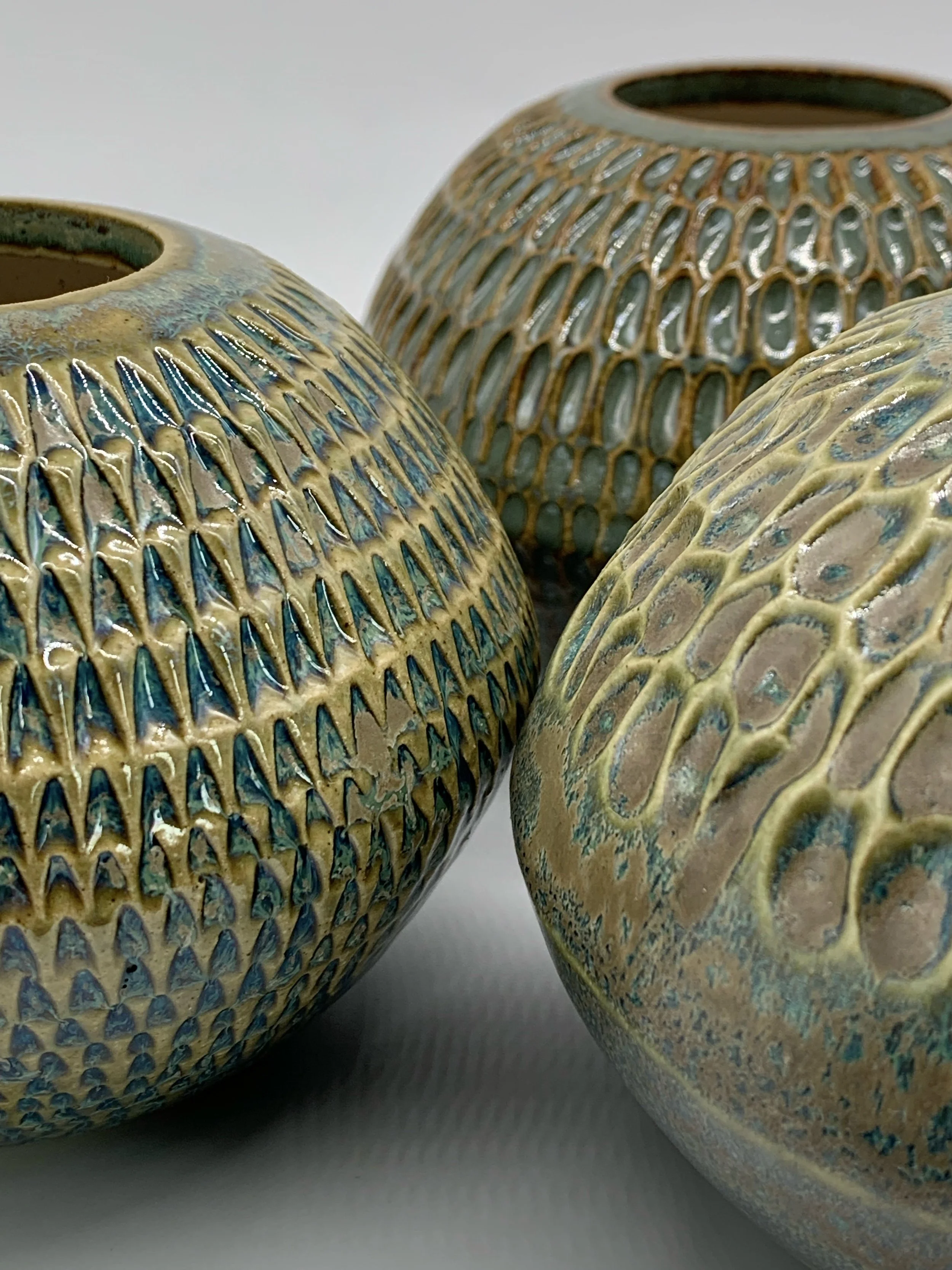 Close-up of three decorative ceramic vases with intricate patterns and textured surface against a plain background.