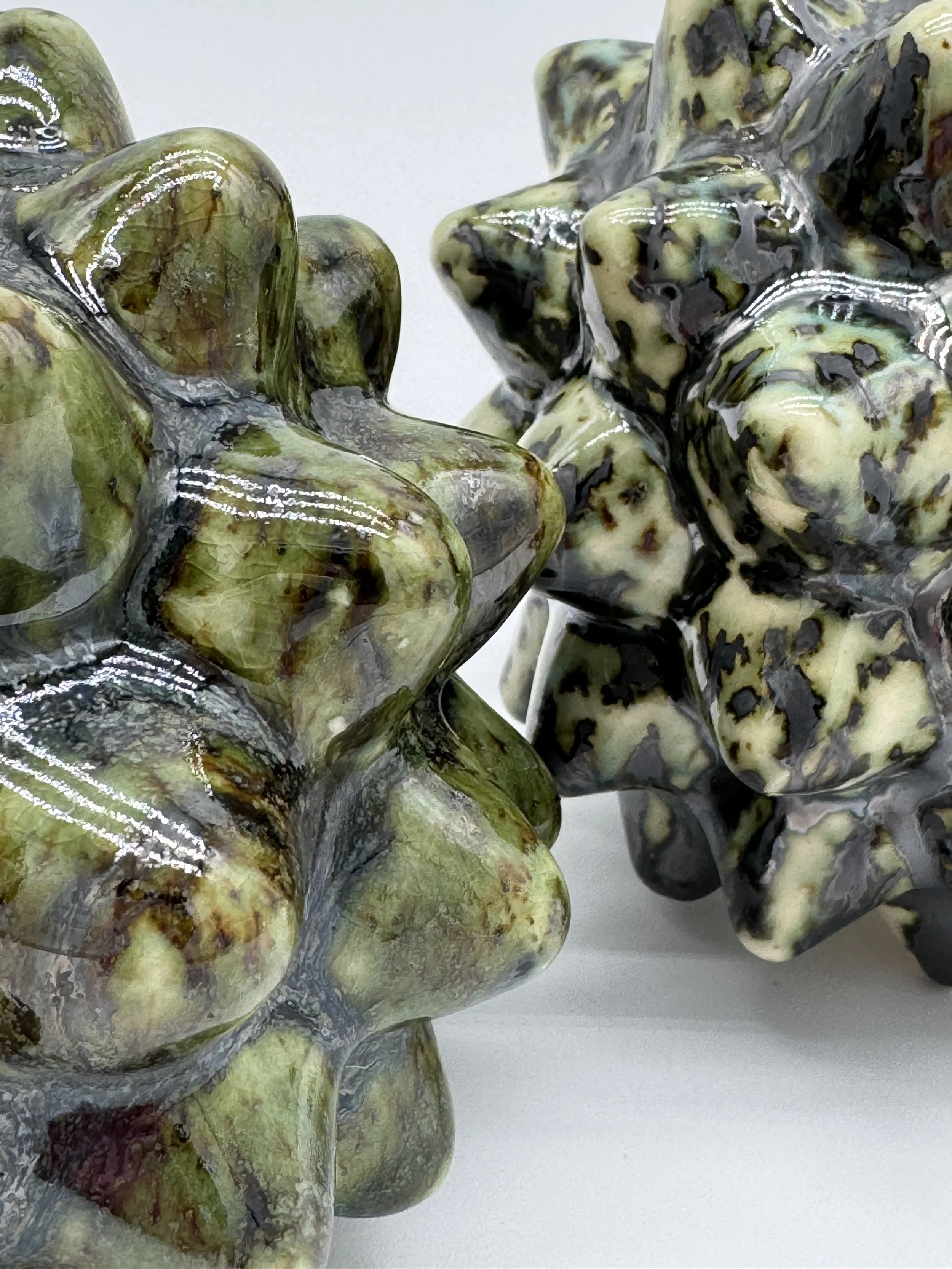 Close-up of two polished stones with green, black, and yellowish patterns, possibly jasper, on a white surface.