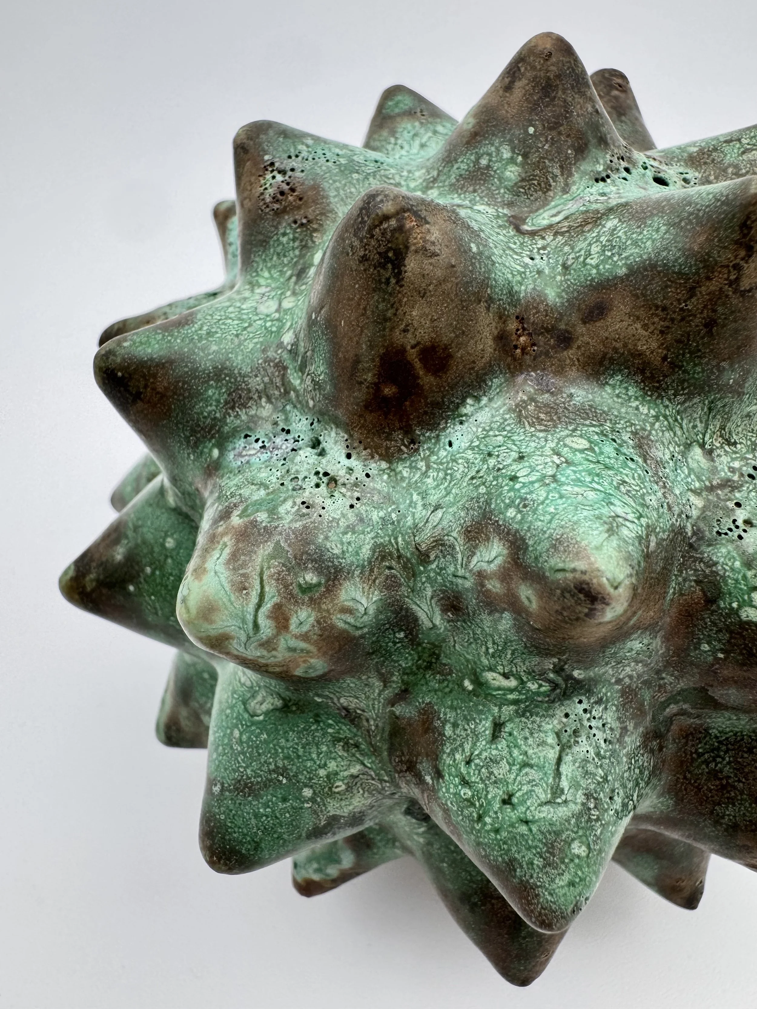 A ceramic sculpture with irregular, spiky surfaces painted in shades of green and brown.
