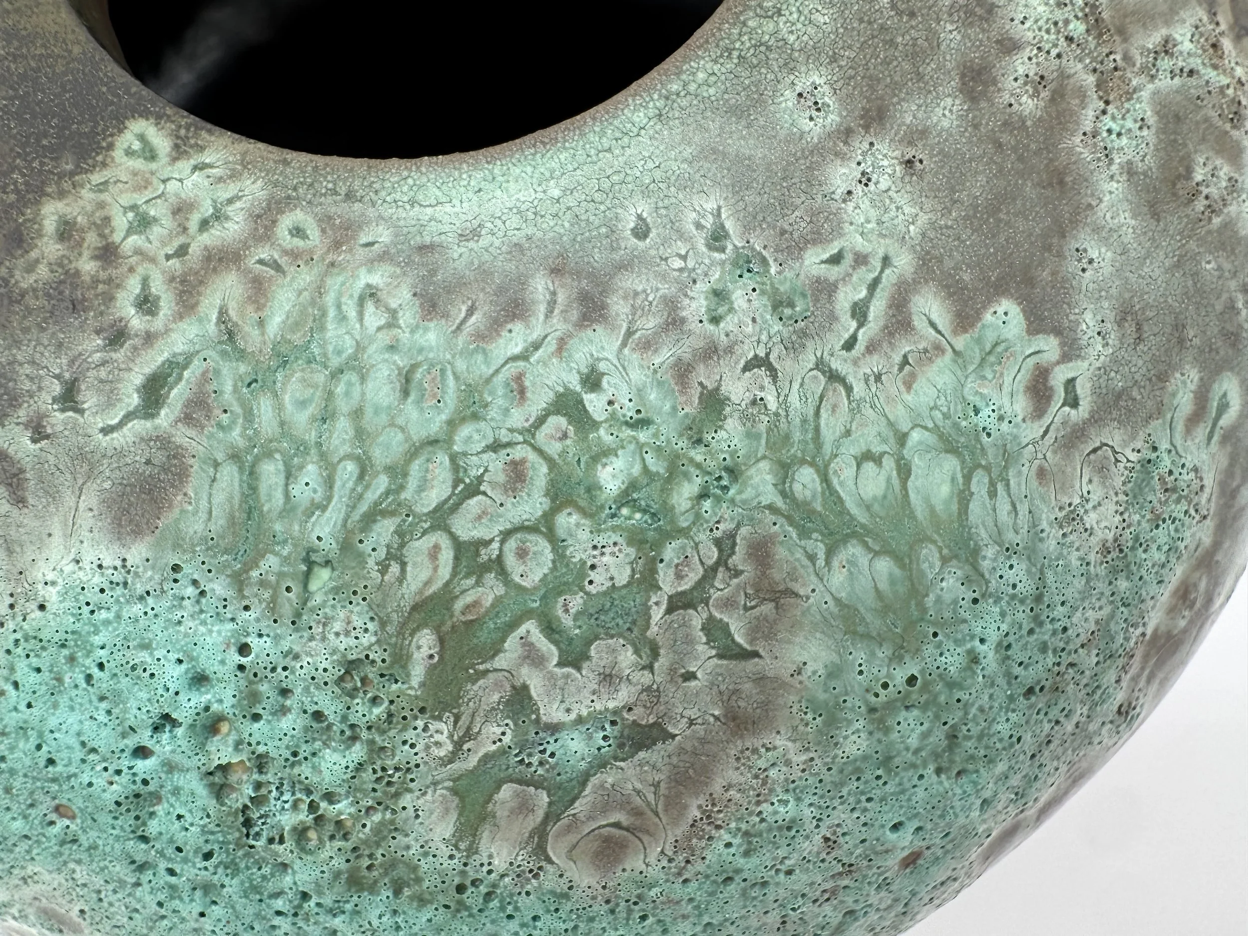 Close-up of a textured, multicolored surface with shades of green, brown, and blue, resembling abstract art or a mineral formation.