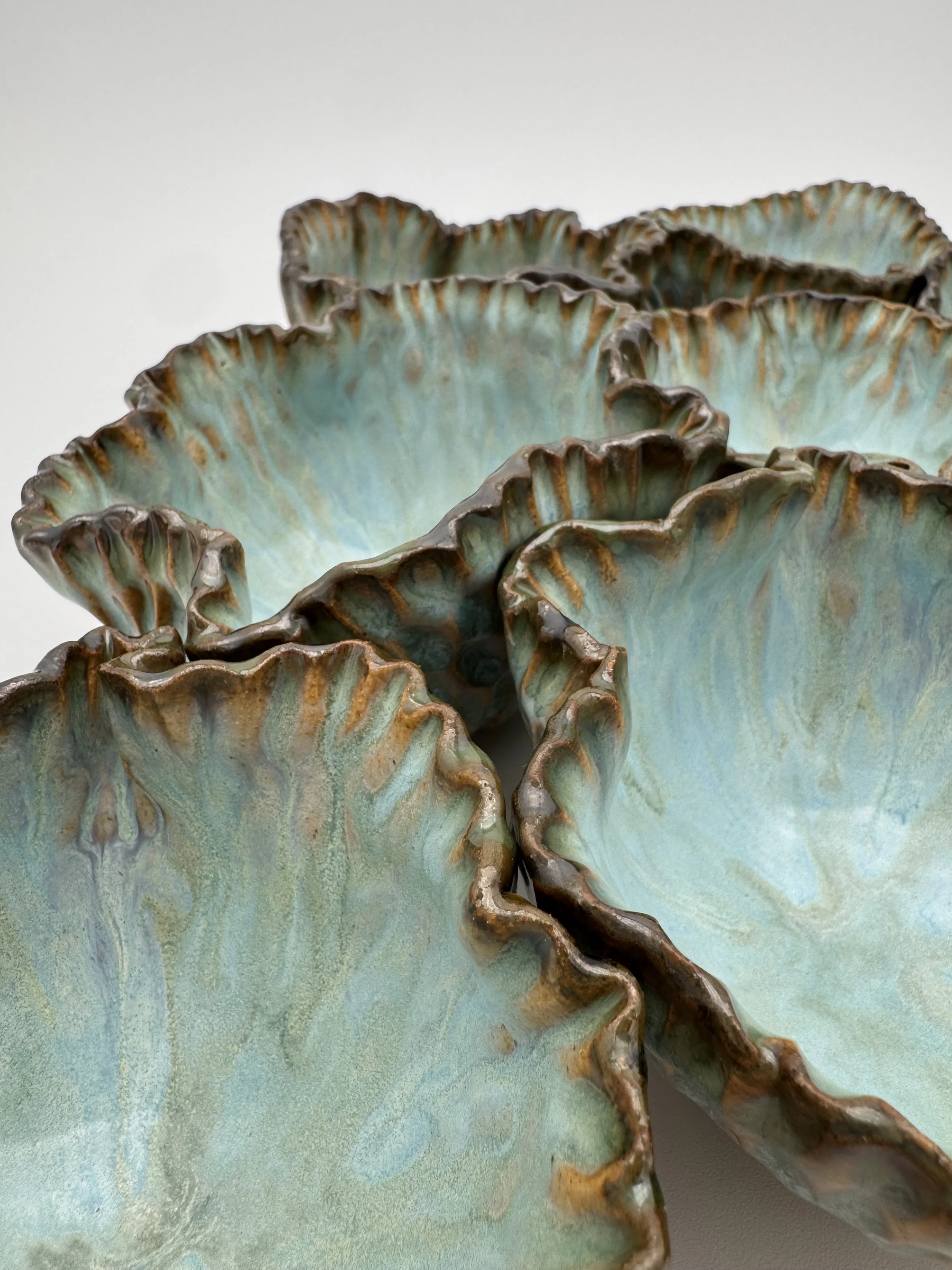 Close-up view of a decorative ceramic bowl with ruffled edges and a greenish glaze with brown accents.