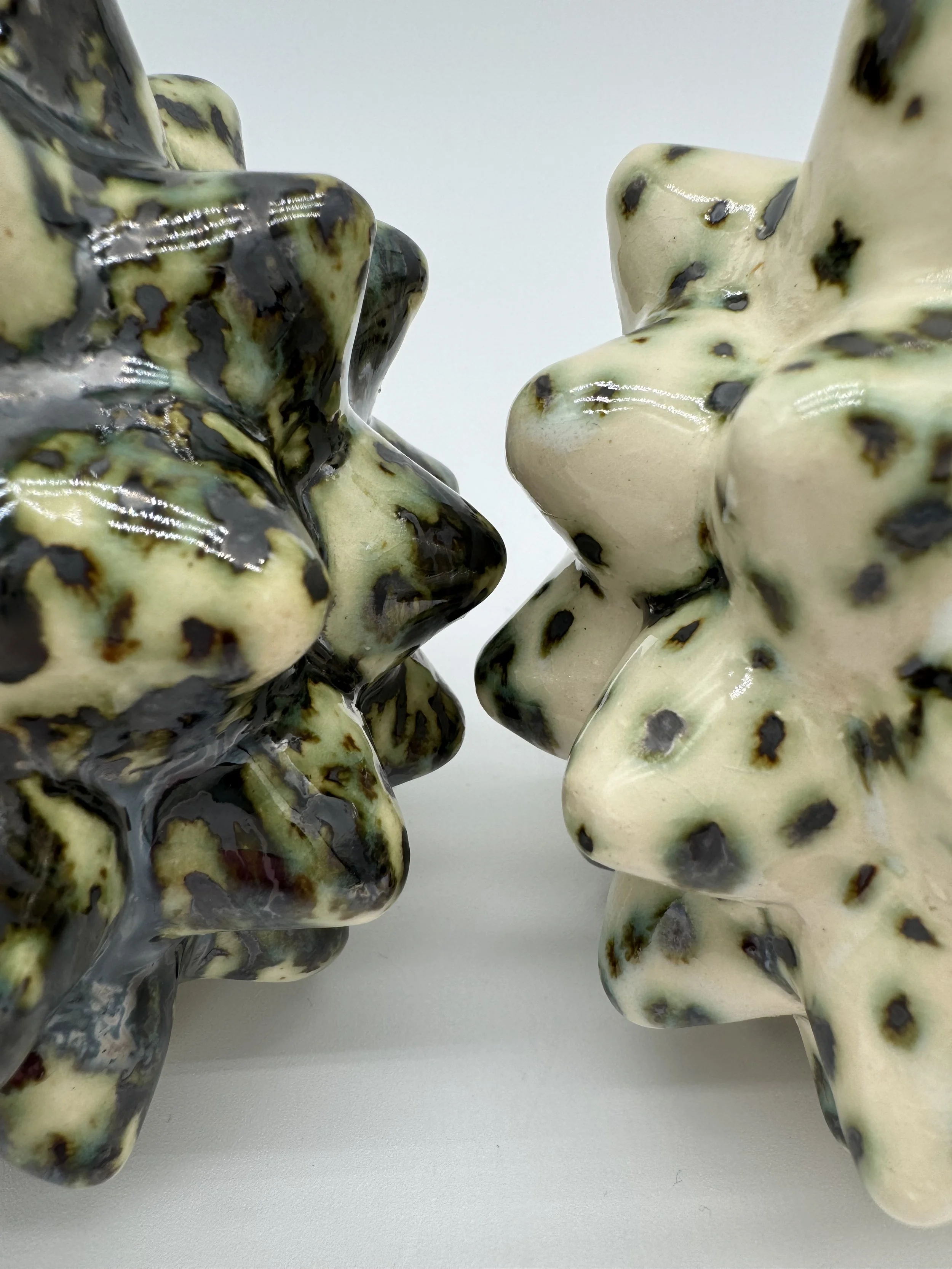 Close-up view of two ceramic sculptures of male torsos, one in black and yellow glaze, the other in white with black spots, shown against a plain white background.