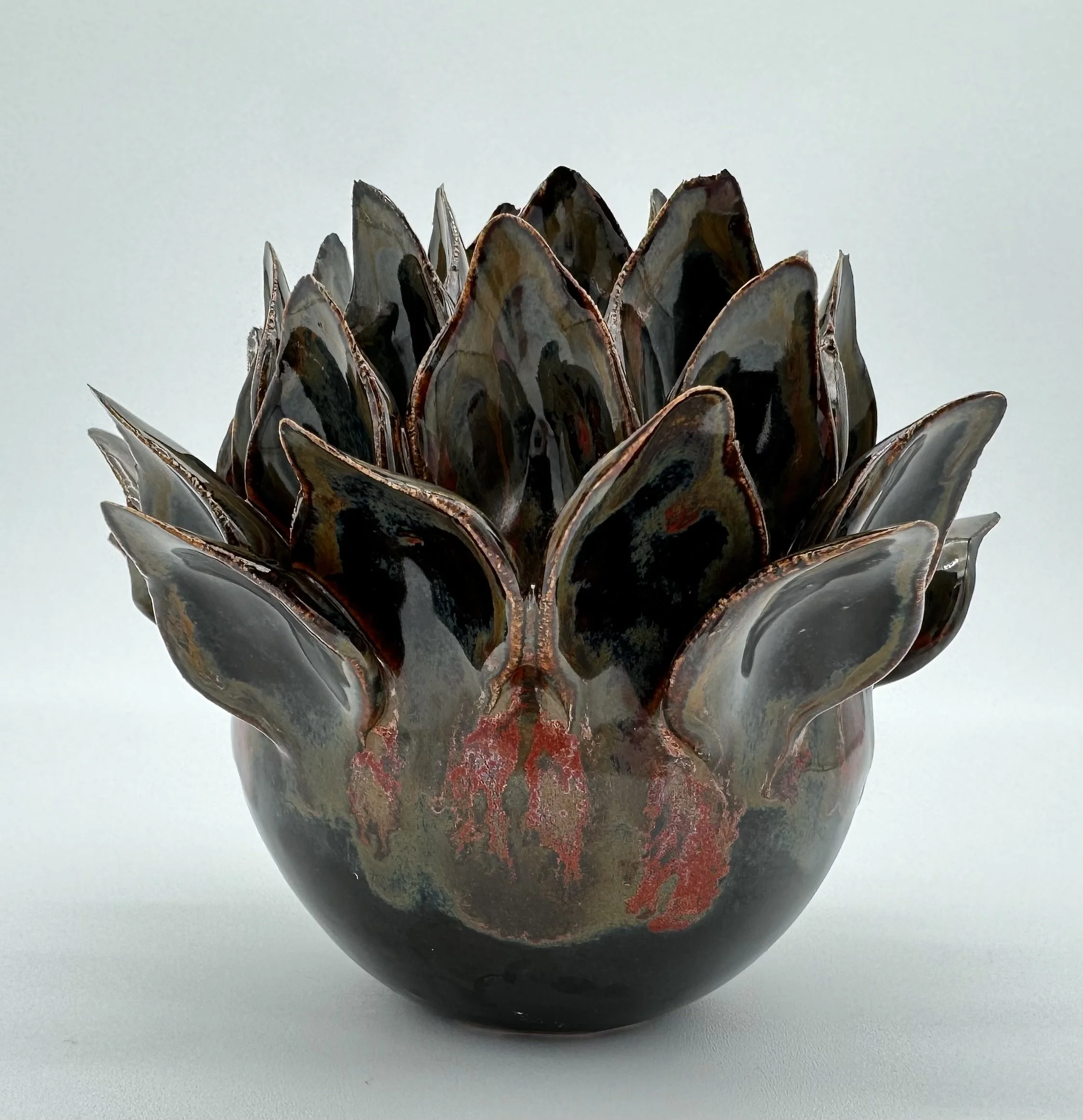 Close-up of a crafted metal sculpture resembling sedum flower with layered petals, dark gray with copper edges, set against a plain light background.
