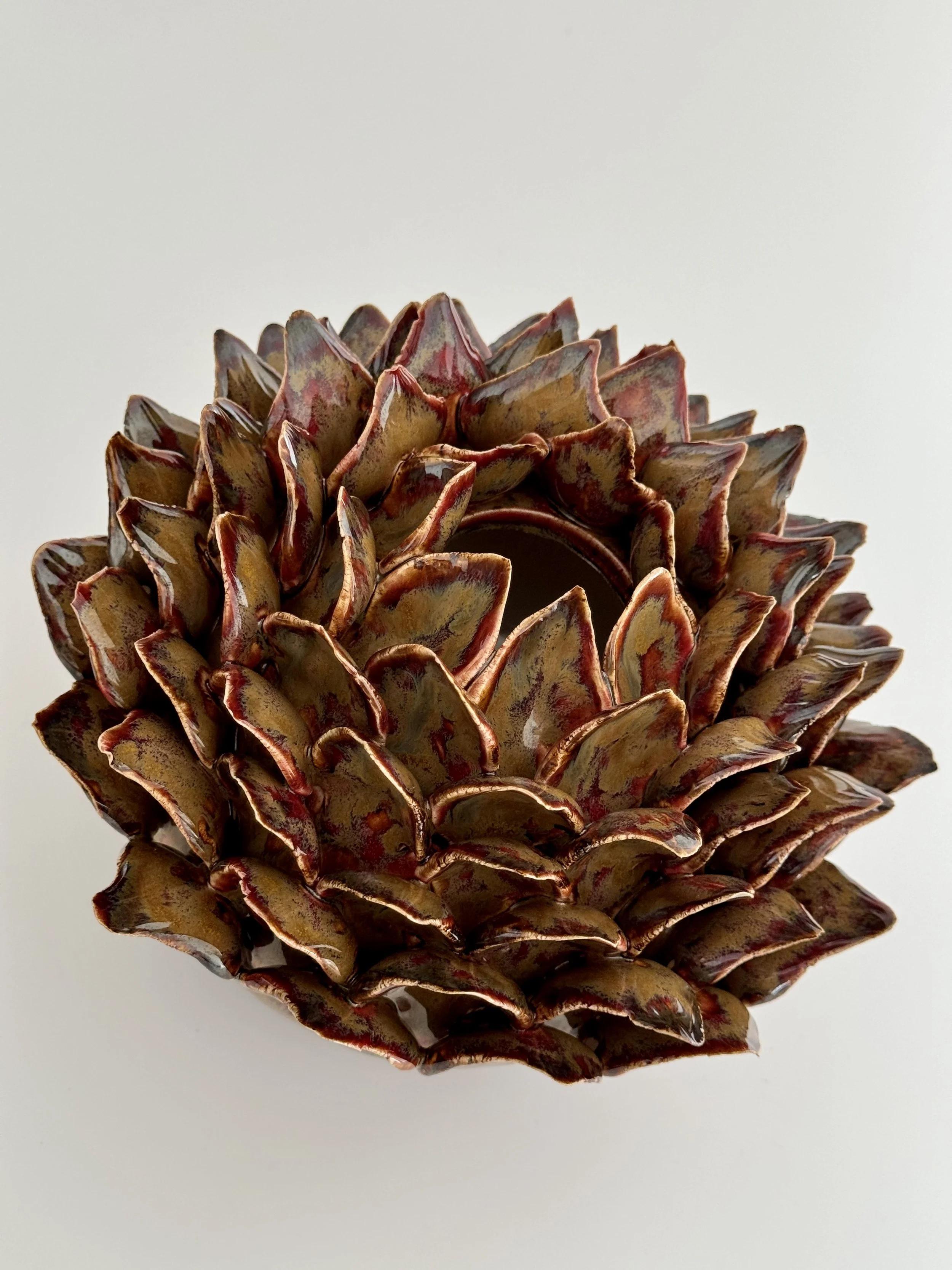 Close-up of a decorative pinecone with a reflective surface, displaying shades of brown and reddish hues, against a plain white background.