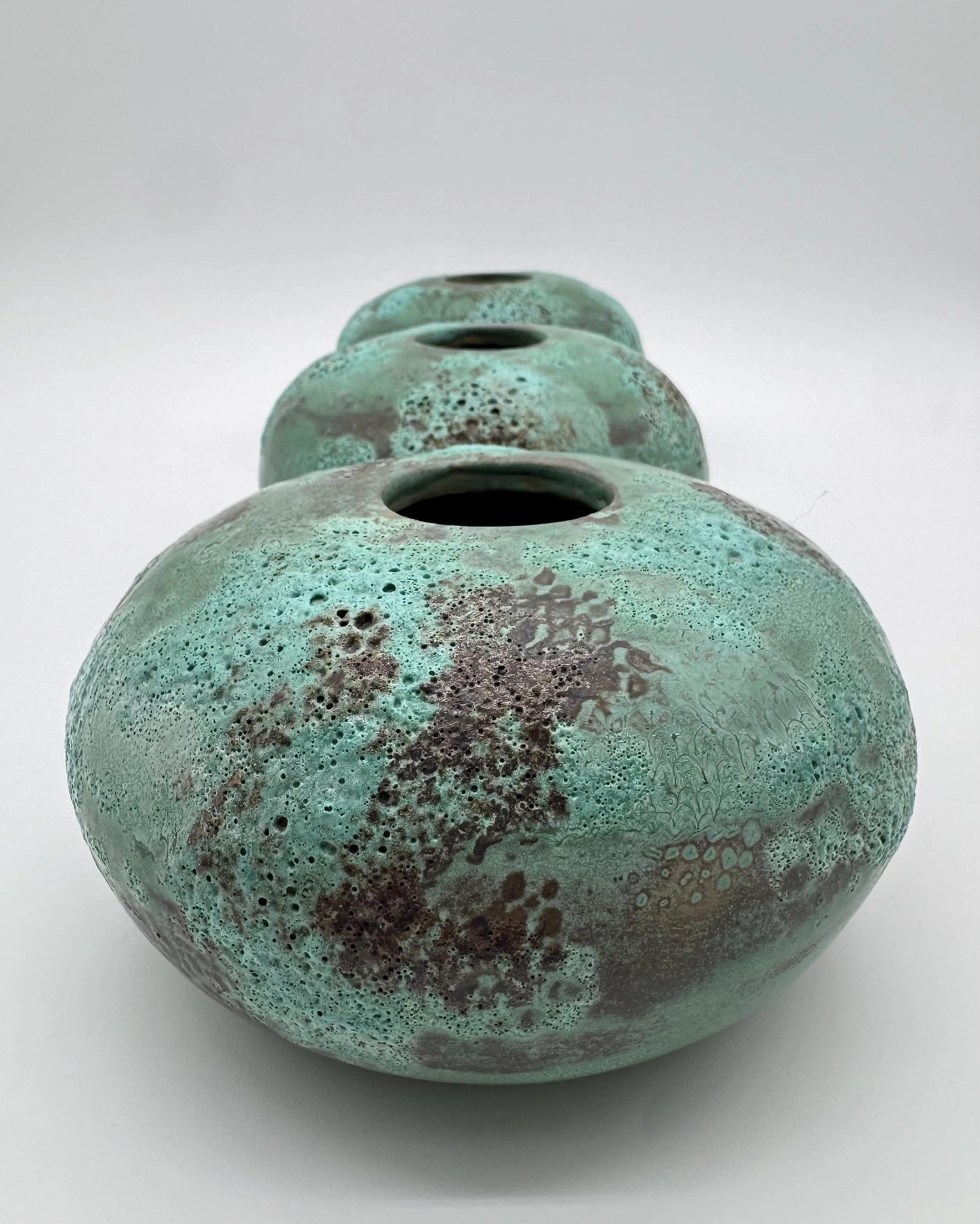 Close-up of four stacked spherical objects with textured, greenish-blue surfaces and dark holes on the top, set against a plain white background.
