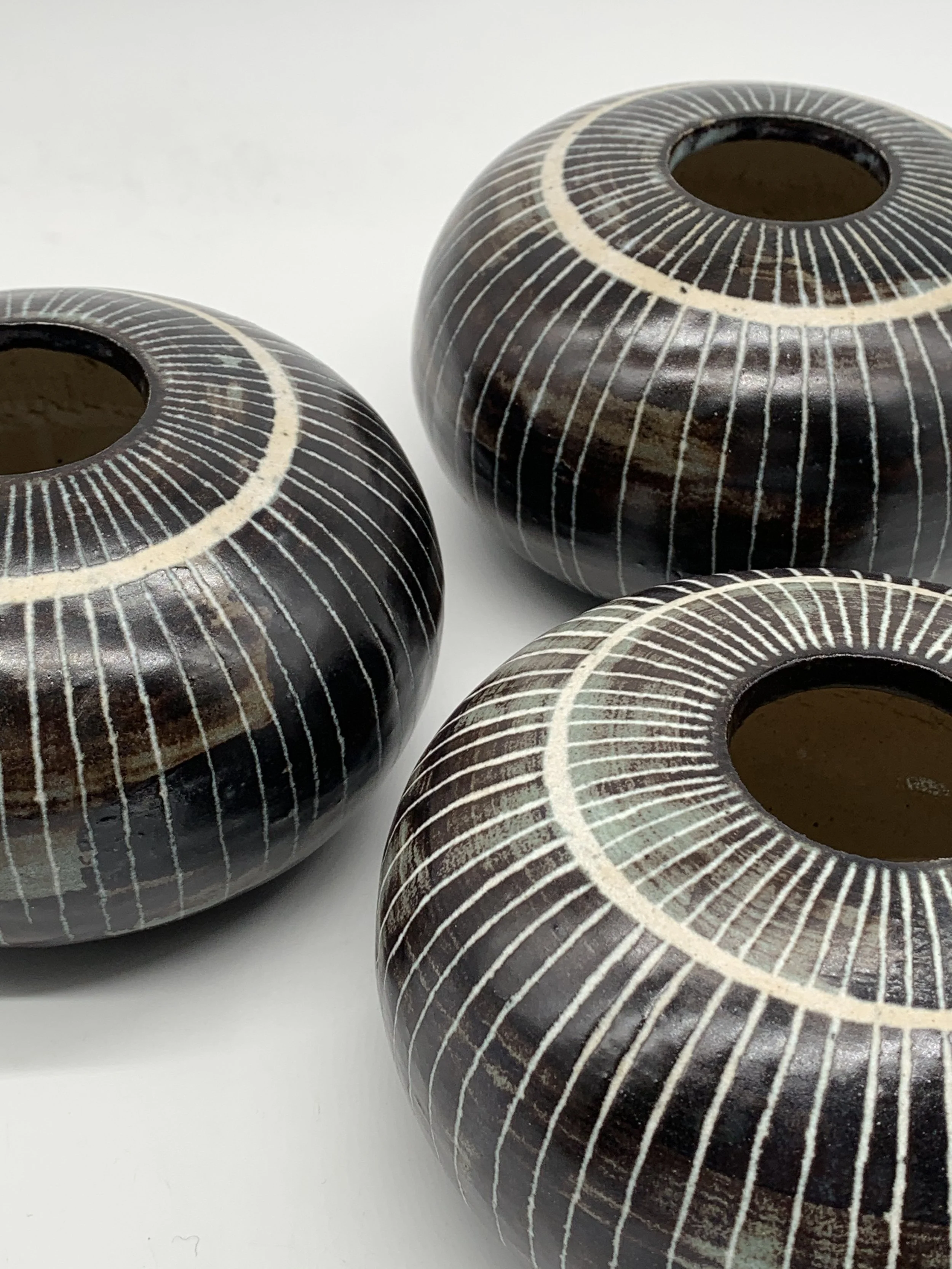 Three ceramic vases with black backgrounds and intricate white circle and line patterns, positioned on a white surface.