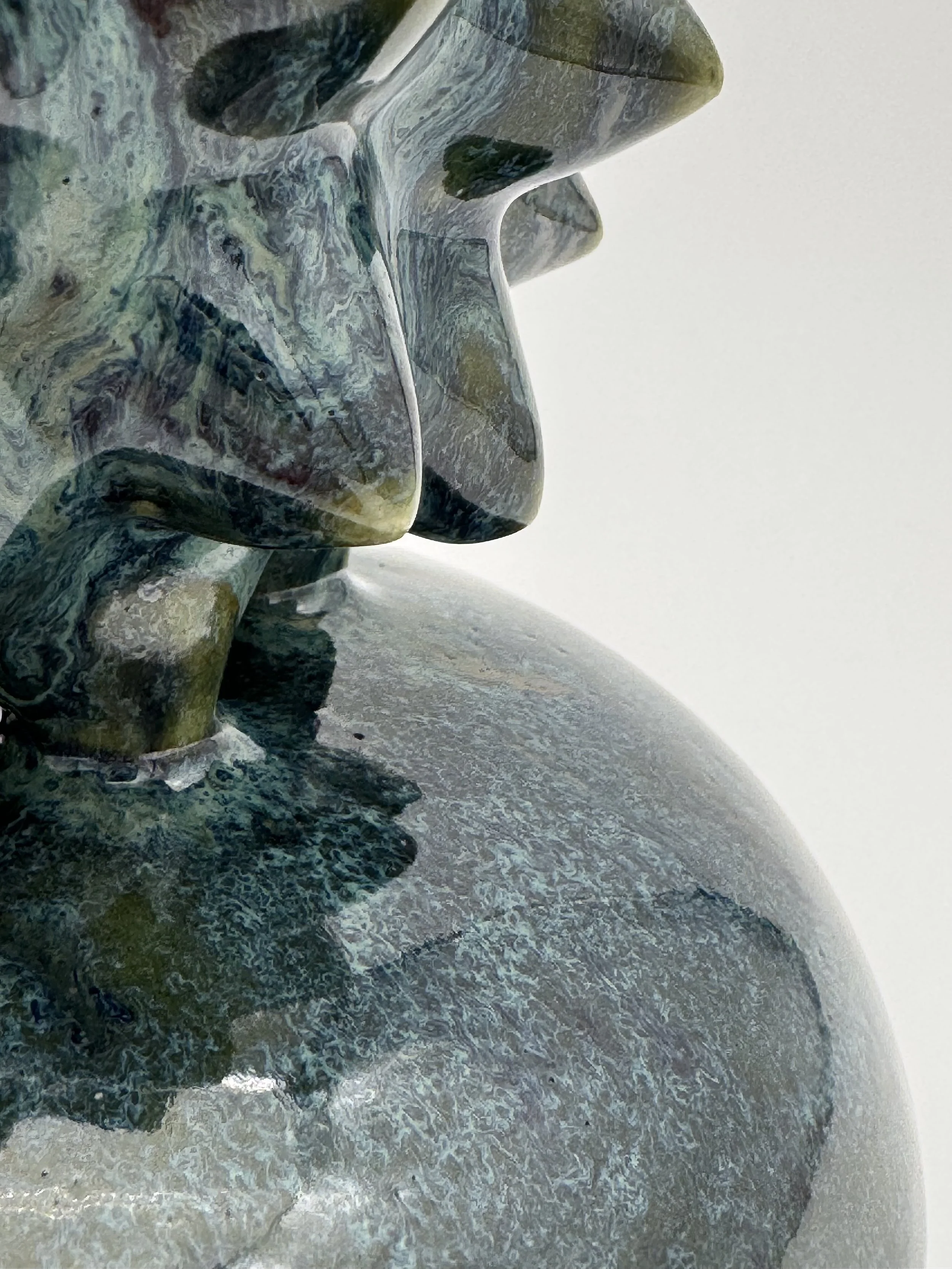 Close-up of a detailed, textured stone sculpture depicting human faces and heads, with intricate carving and patterns.