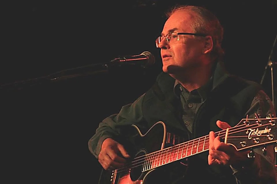 Glenn Williams playing acoustic guitar and singing into a microphone