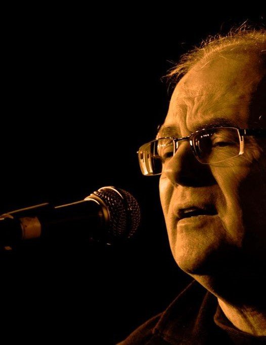 Close-up of Glenn Williams singing into a microphone on a dark stage.